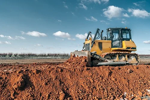 A yellow bulldozer working on a large dirt area under a partly cloudy sky.