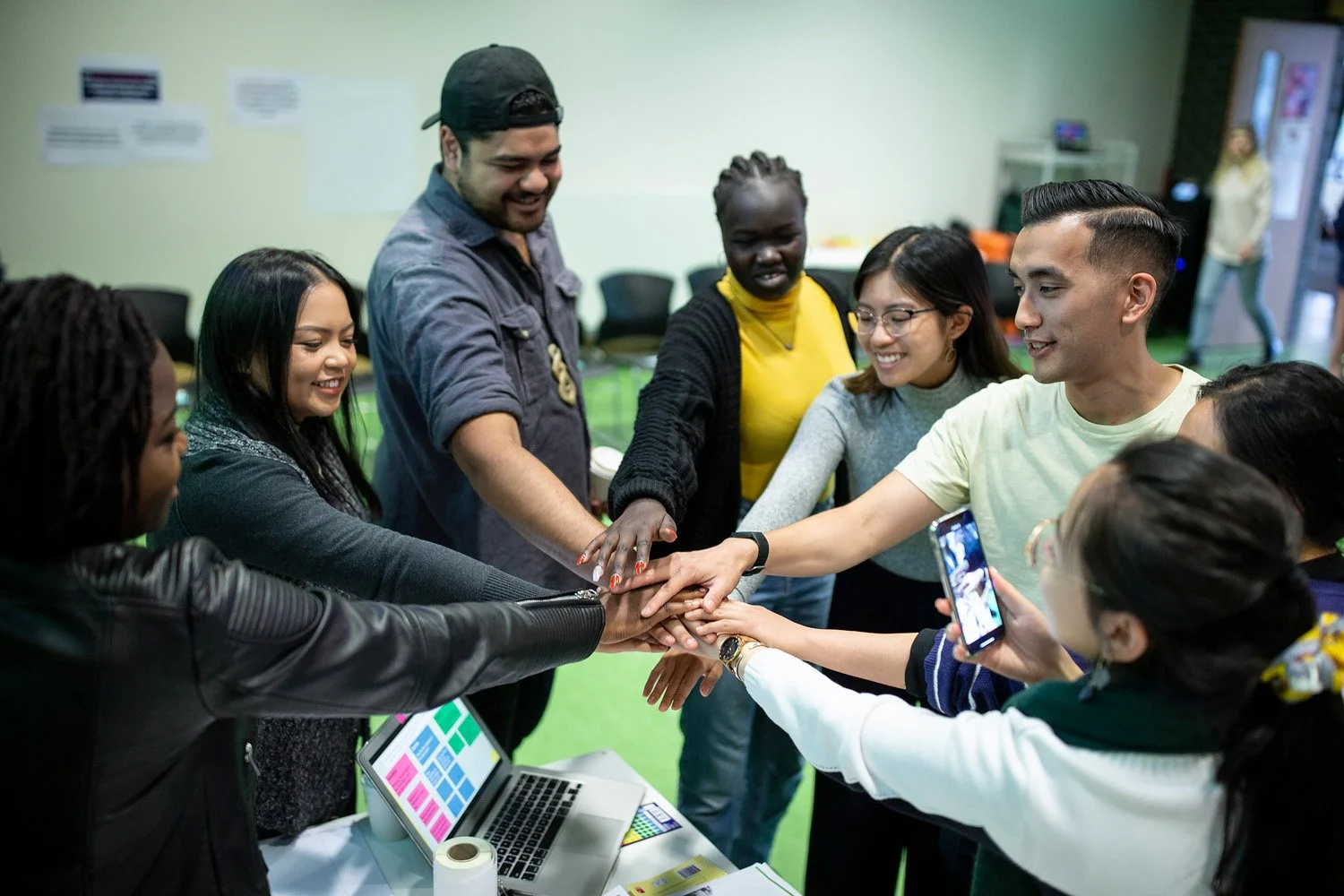 Eight people from the Project BrIMPACT team are smiling in a circle with their hands touching in the centre.