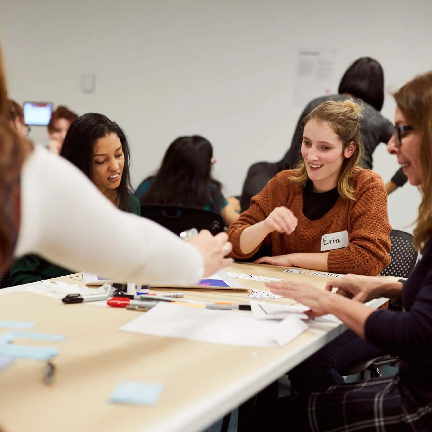 A group of people are sitting at a table, participating in a co-design workshop. They're smiling and chatting while focused on the sheets of paper scattered on the table.