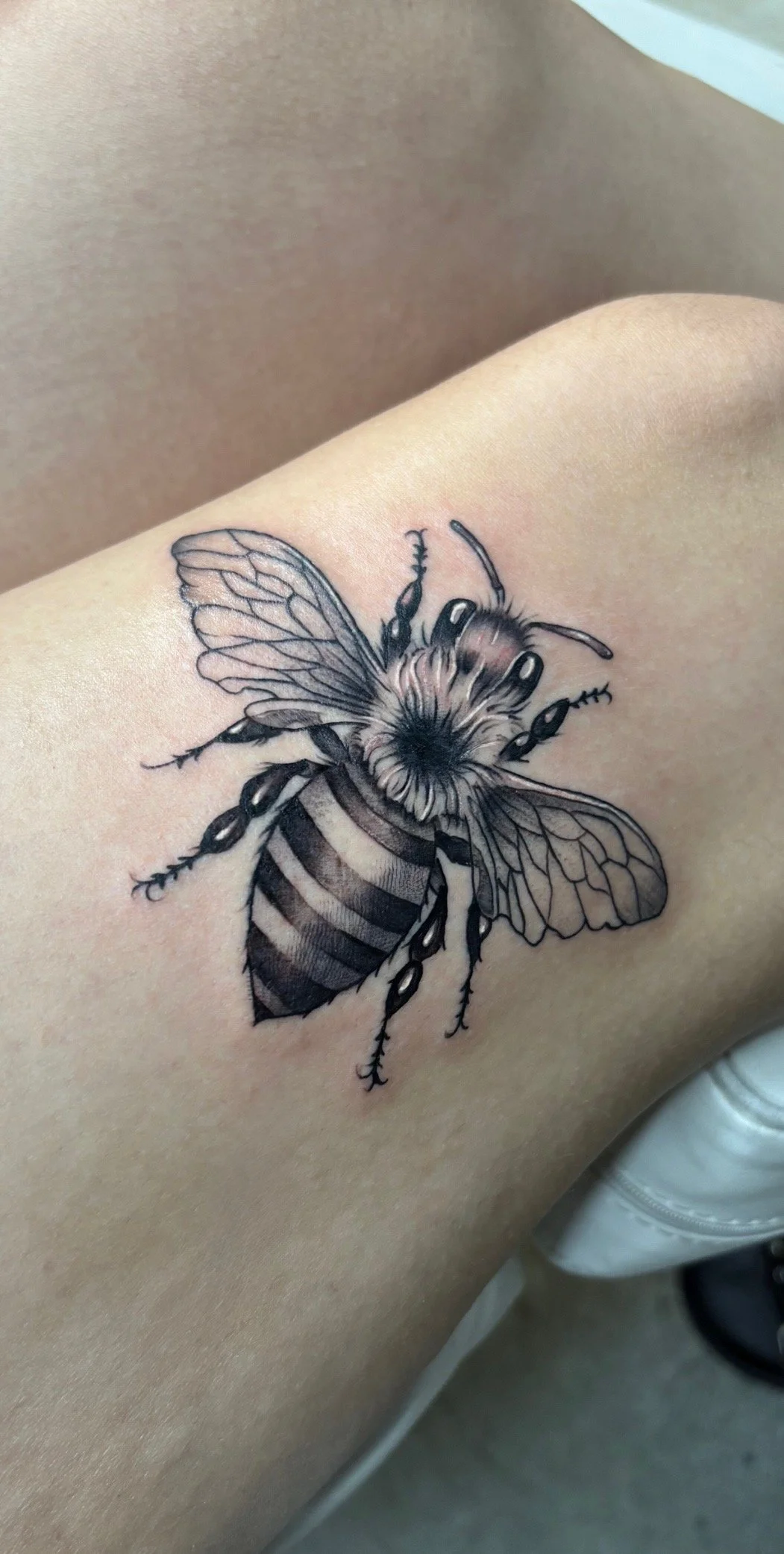 Black and gray tattoo of a bee on person's skin showing detailed wings, stripes, and antennae.