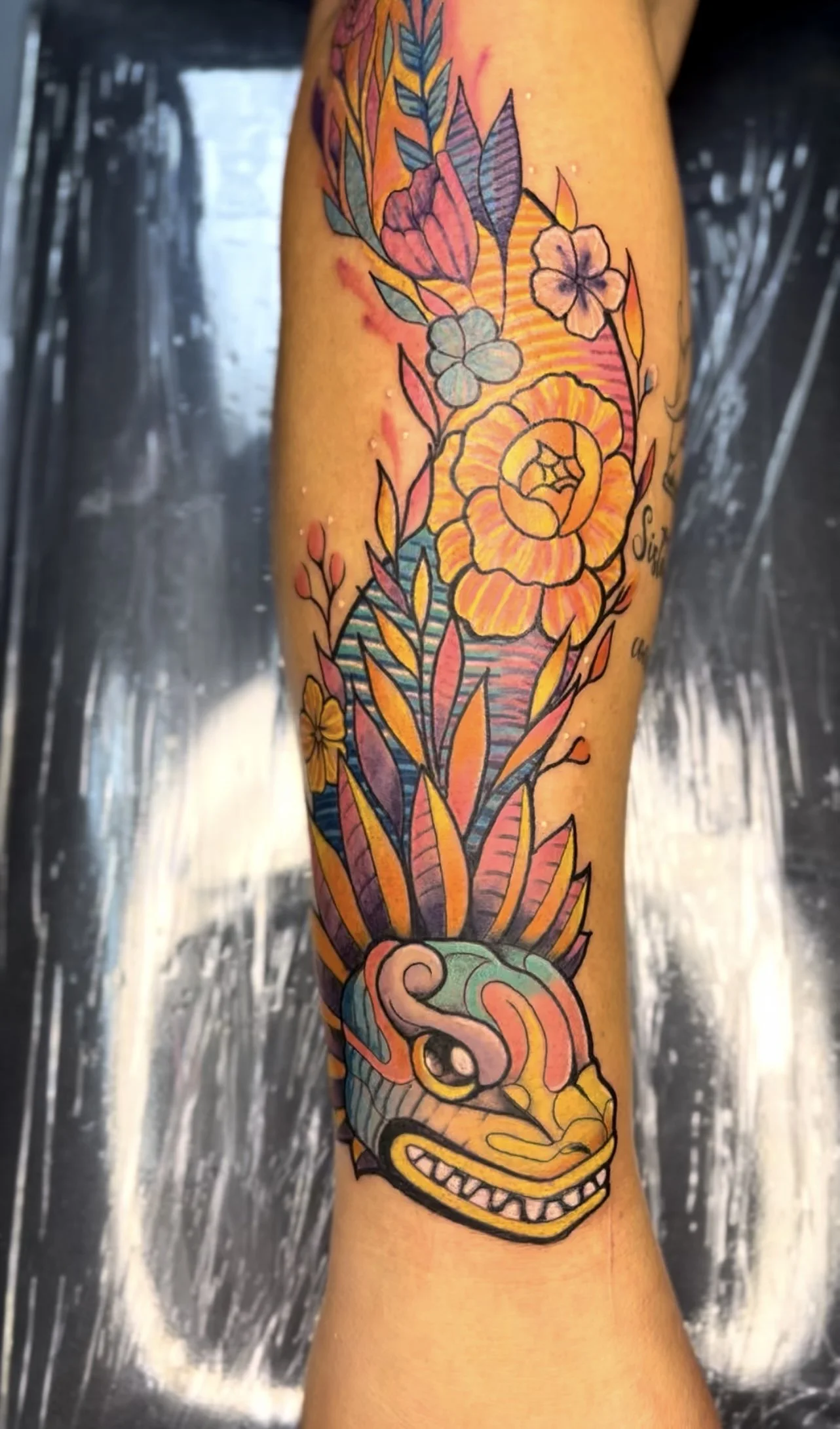 A colorful tattoo of a dinosaur head with floral elements on a person's arm, featuring vibrant colors and detailed linework.