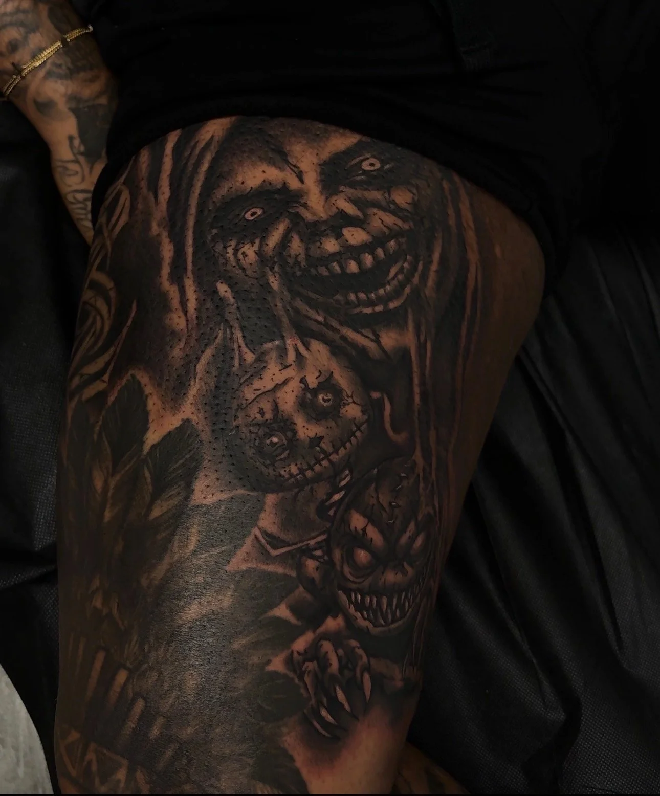 Tattoo of creepy clown faces with exaggerated features on a person's thigh.