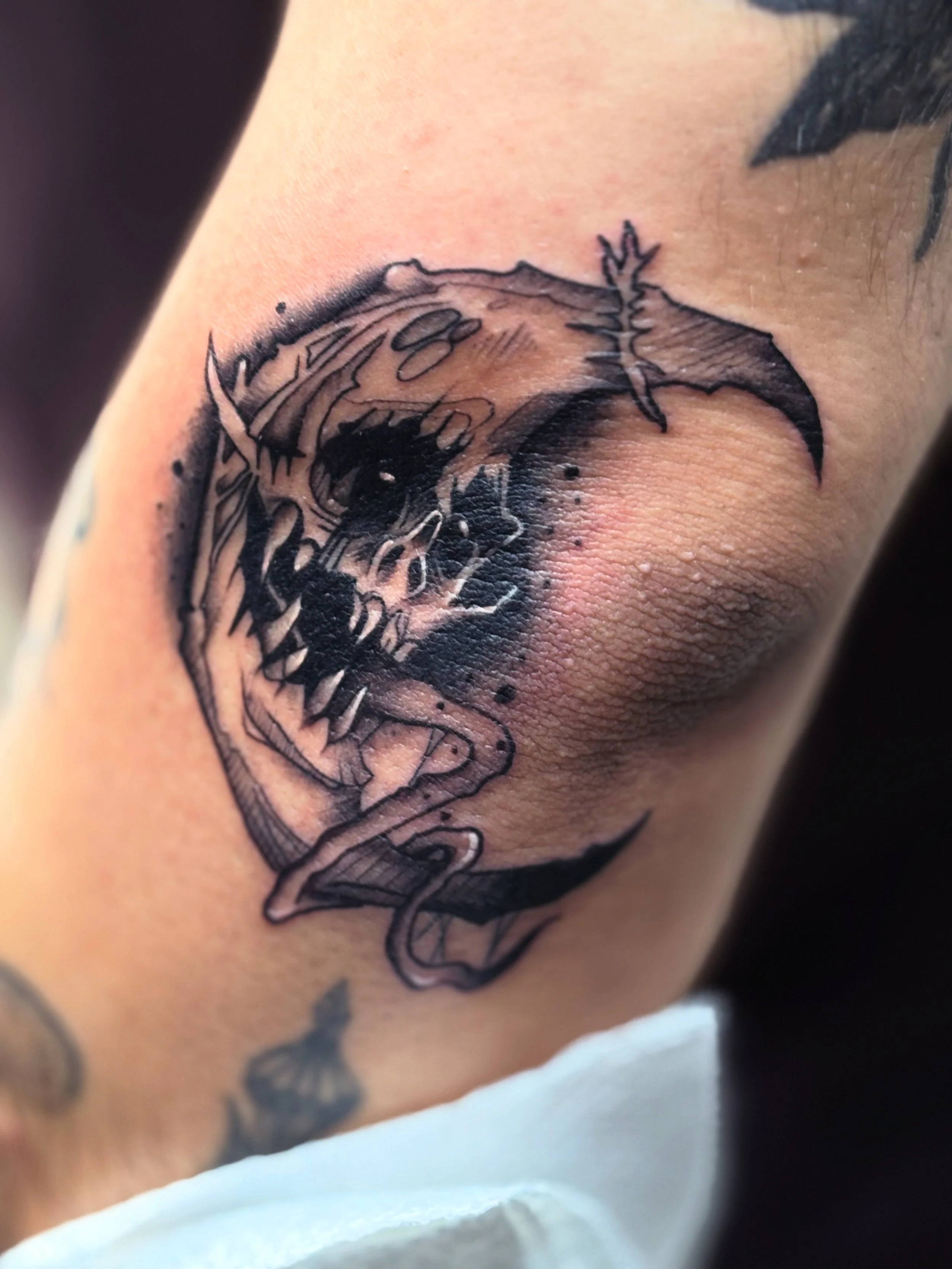 A black tattoo of a moon with a face with detailed fur and sharp teeth on a person's upper arm.
