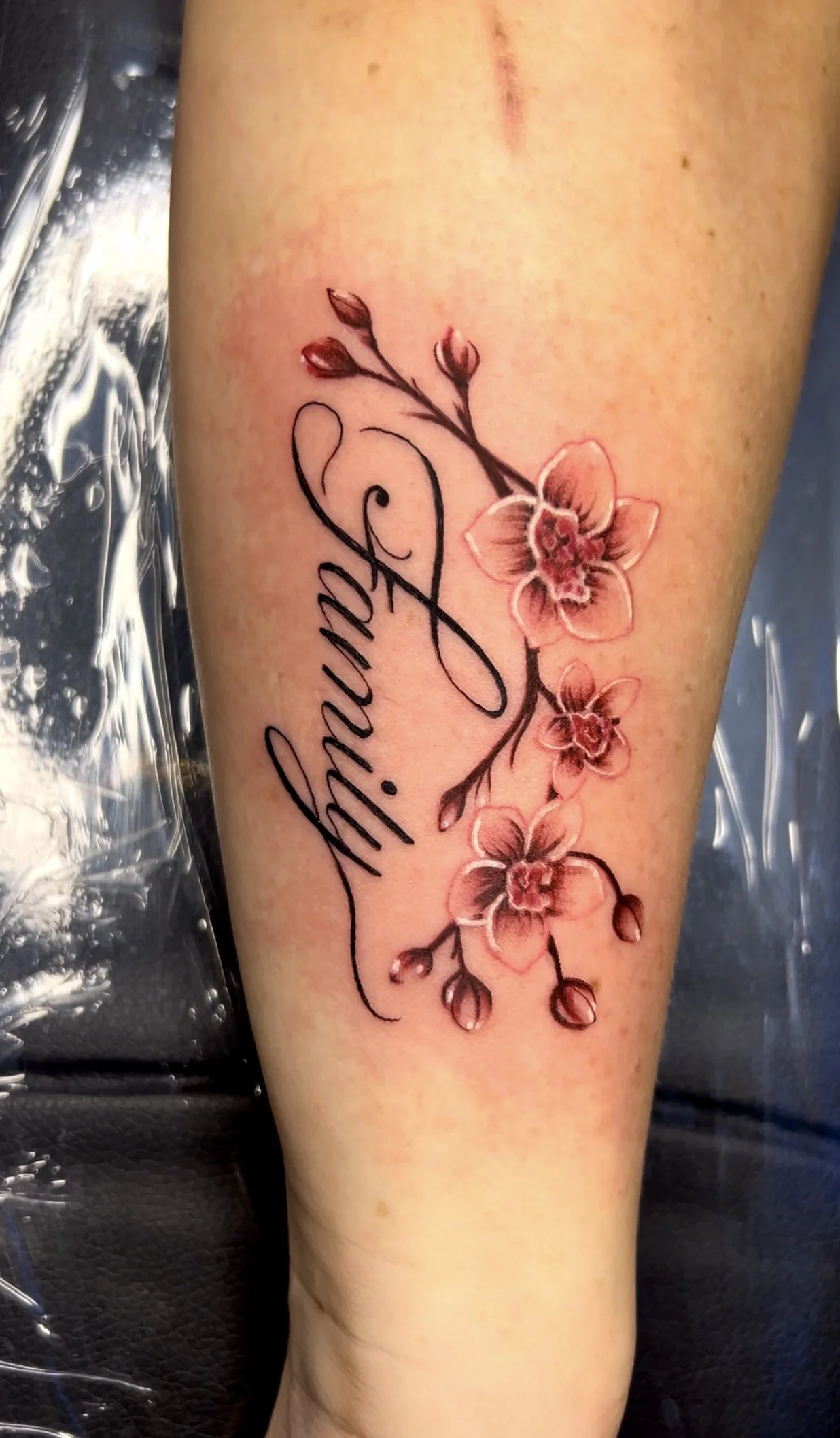 A tattoo of pink orchids with dark outlines, accompanied by a cursive script that reads "Grandma".