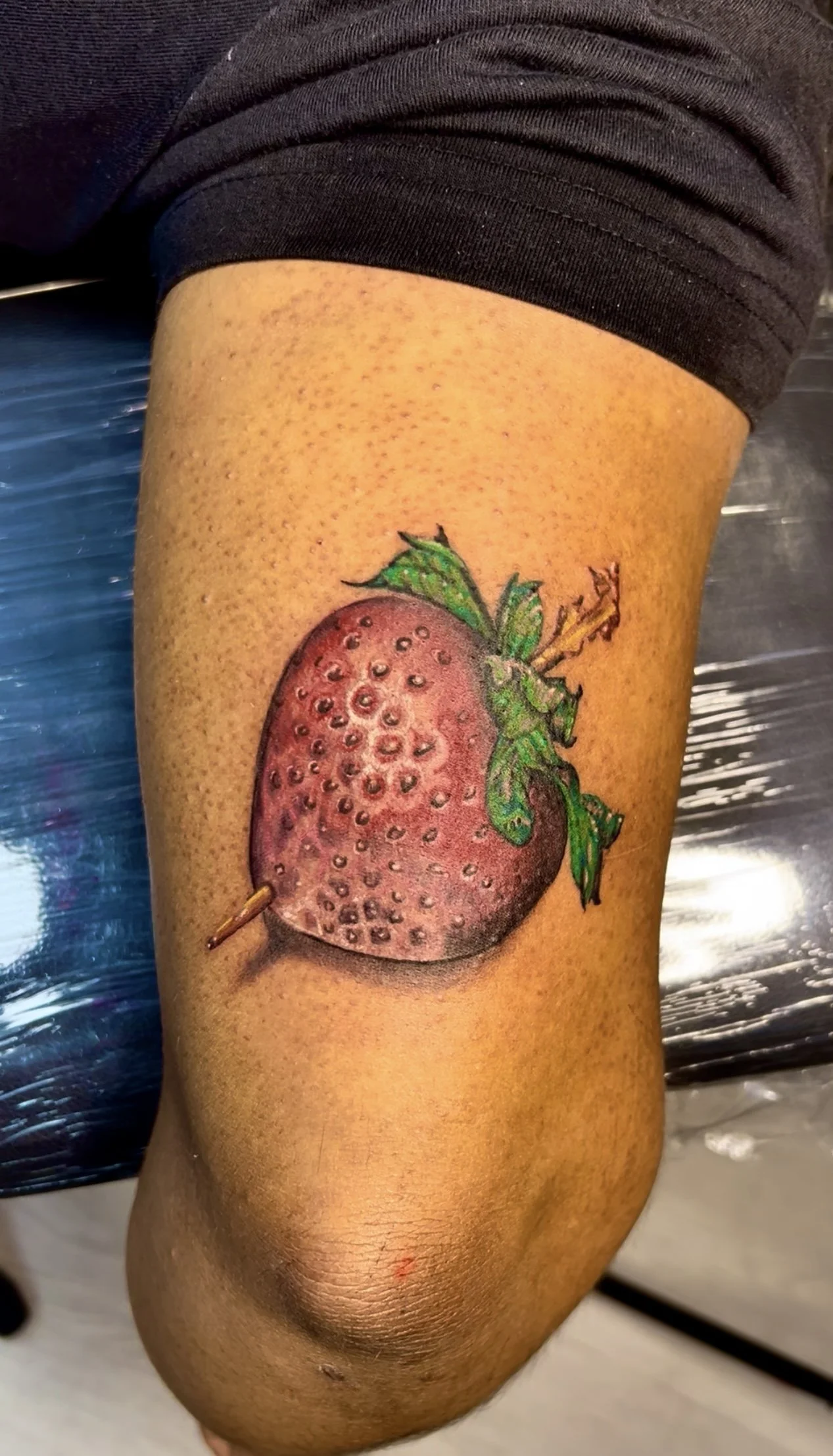 Colorful tattoo of a strawberry with green leaves on a person's arm.