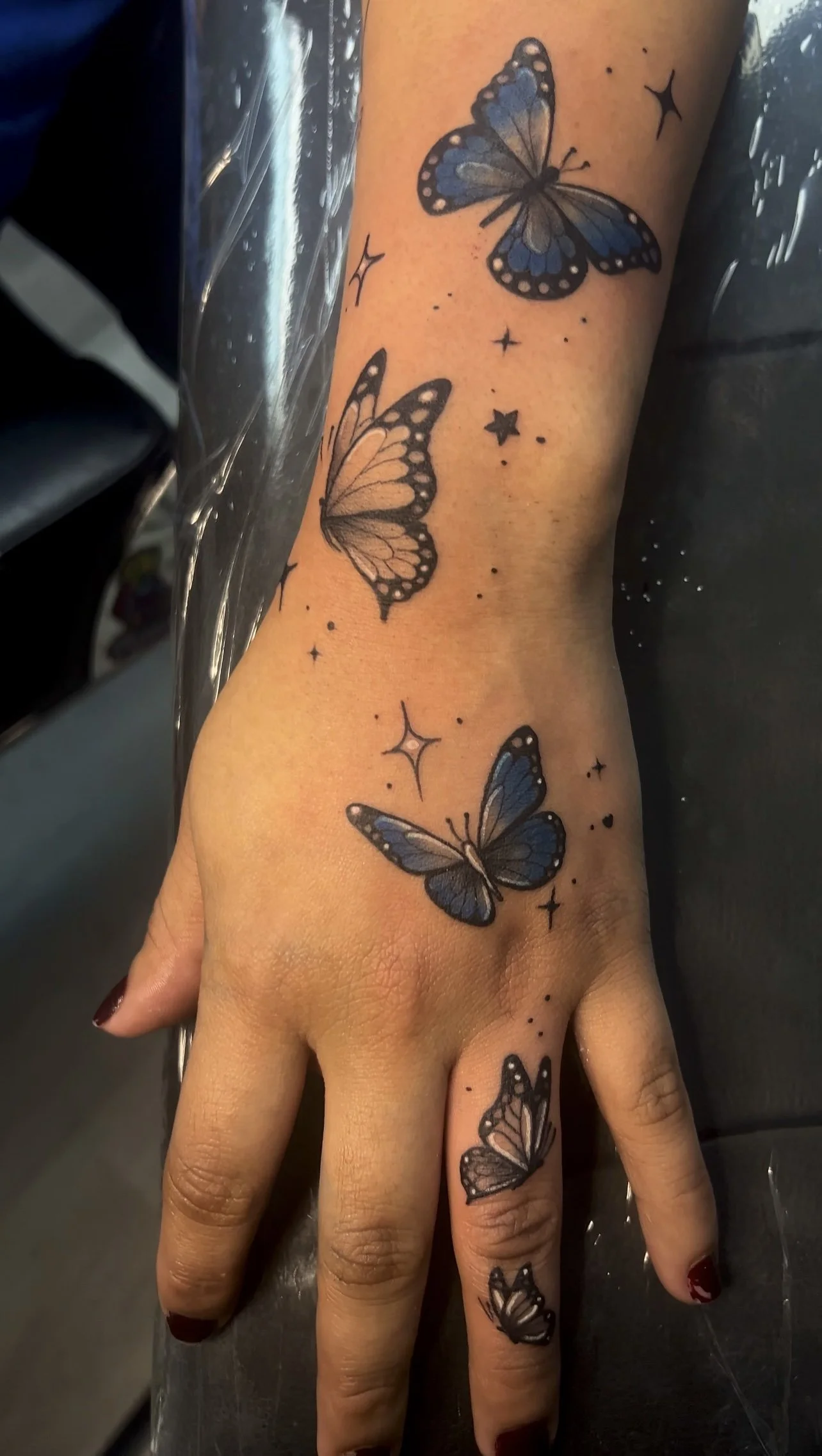 Tattoo of blue and black butterflies with star and sparkles on a person's arm and hand.