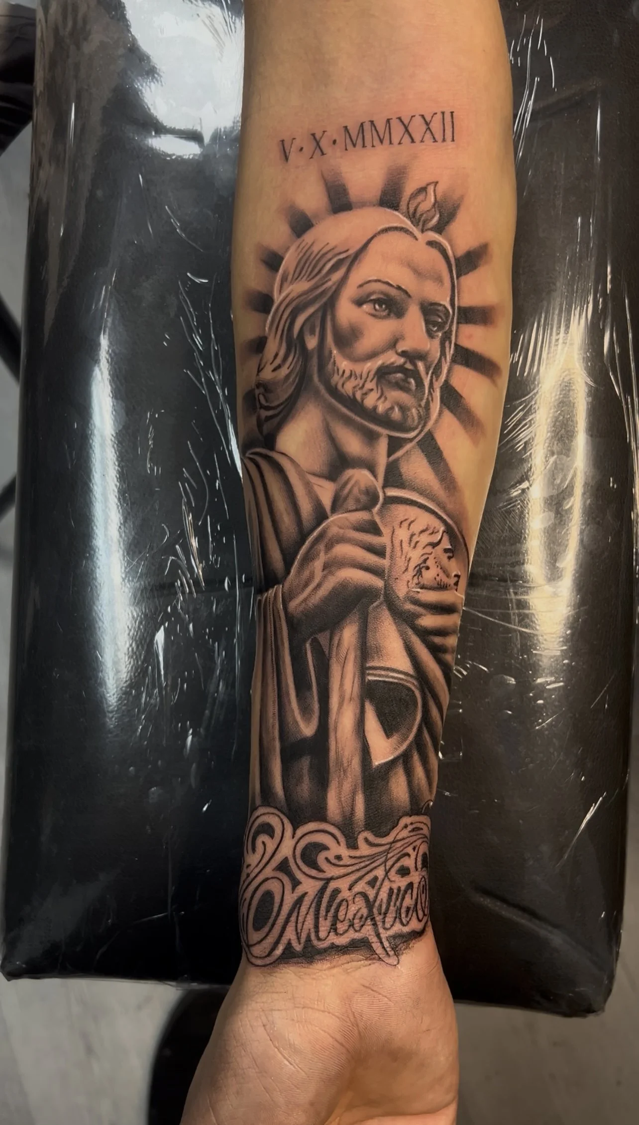 A tattoo of Jesus Christ with a halo behind his head, holding a lion, with the word 'Mexico' written at the bottom and Roman numerals V.X.MMXXII above his head.