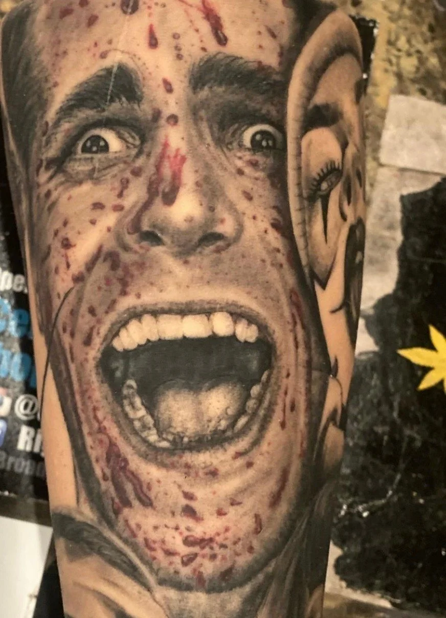 Close-up of a tattoo depicting a face with an angry expression, open mouth, and visible teeth, with detailed shading and skin blemishes.