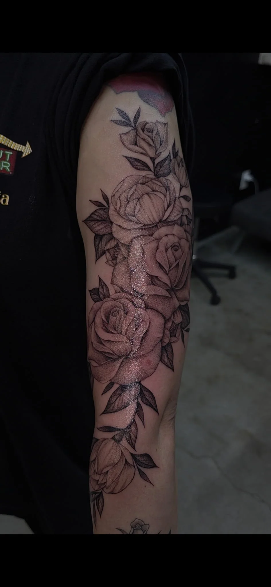 A person's arm with a large, detailed black and gray floral tattoo featuring roses and leaves.