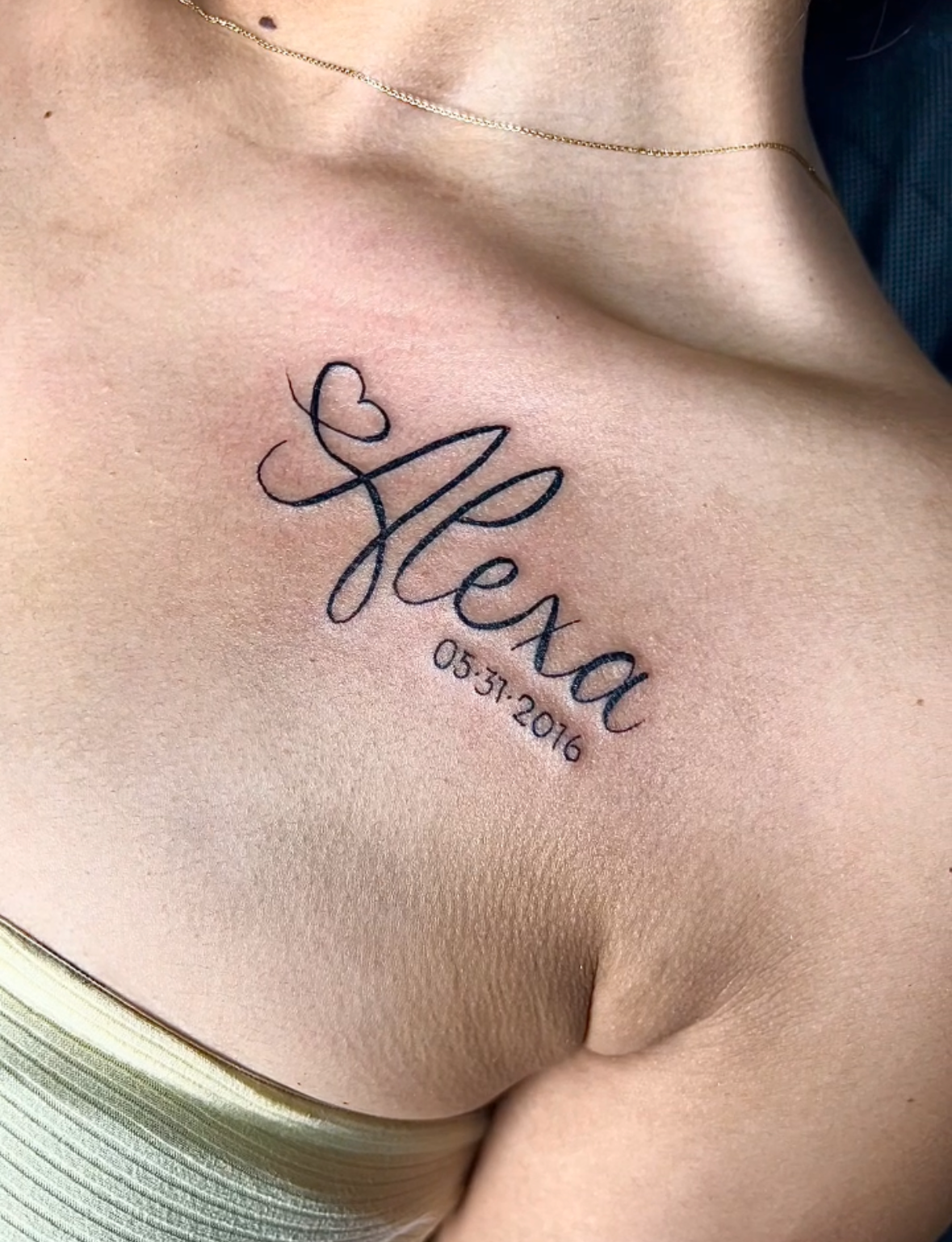 Tattoo on a woman's chest with the name 'Leo' in cursive script, a small heart, and the date 05.31.2016.
