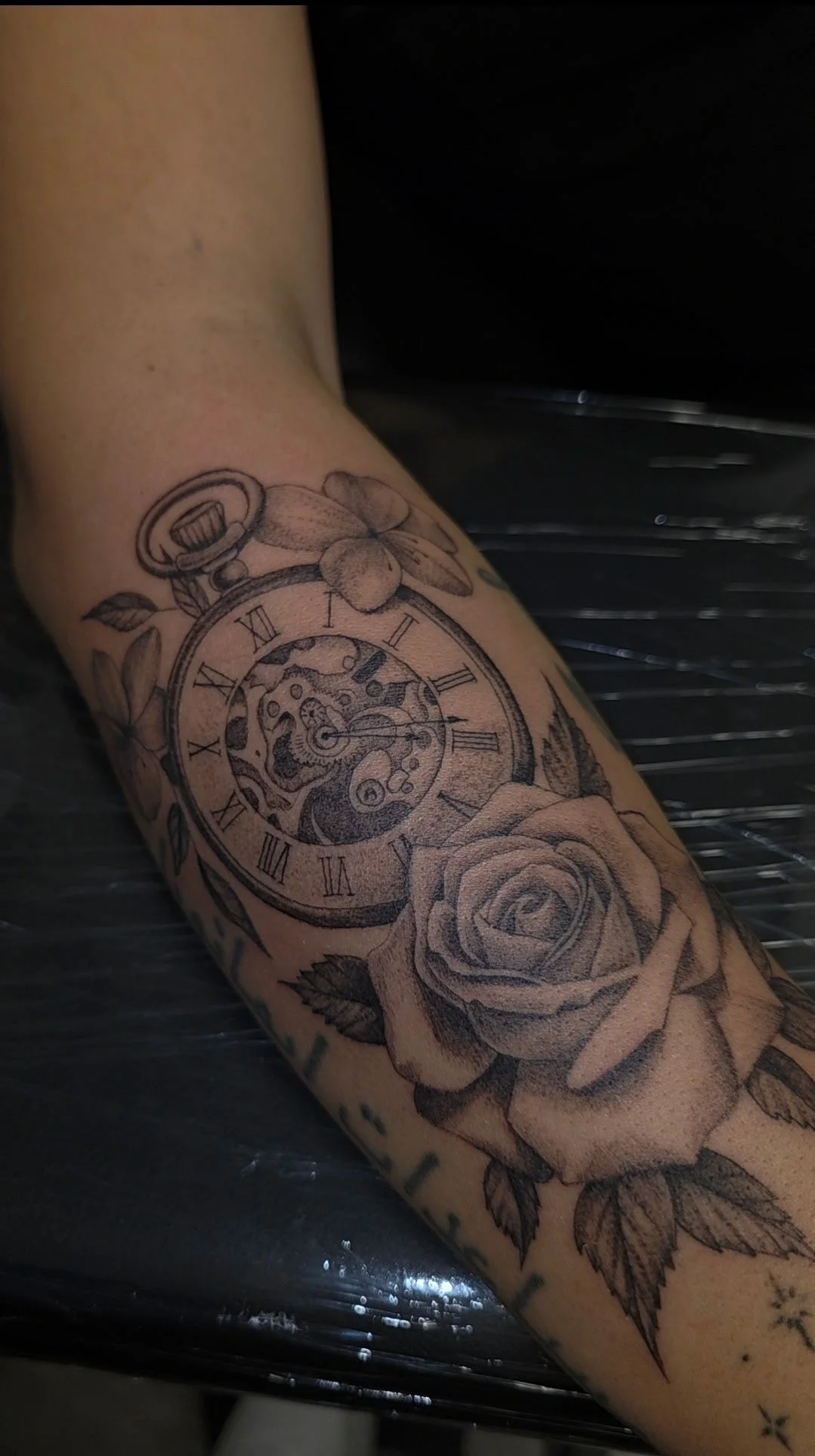 Tattoo of a pocket watch and roses on an arm.