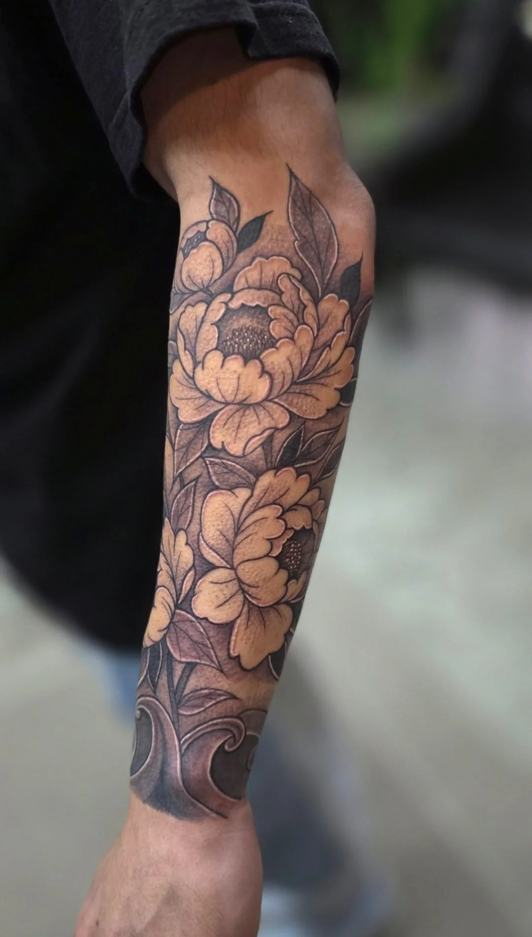 A tattoo of large, detailed flowers and leaves on a person's forearm.