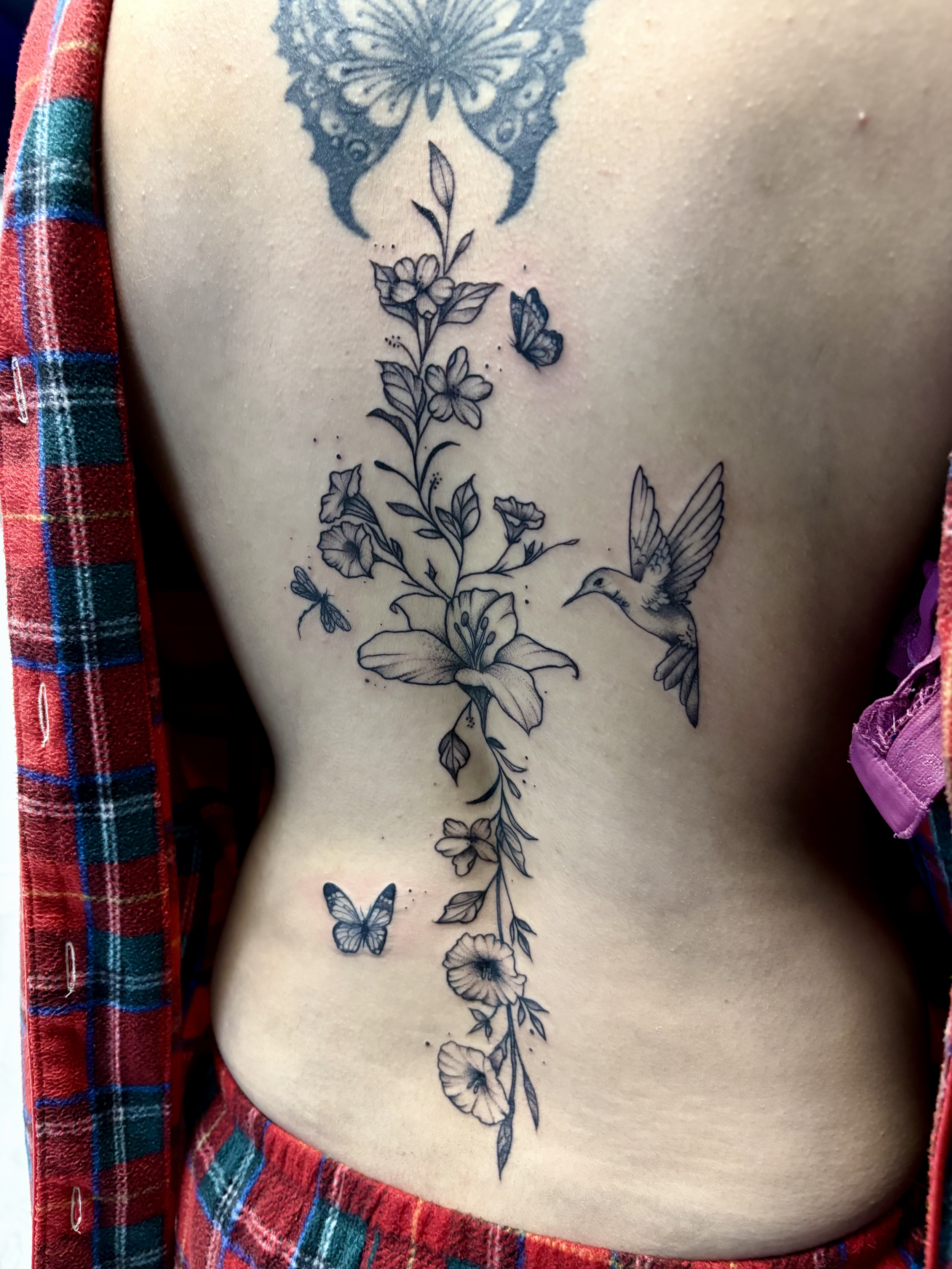 Black floral tattoo with hummingbirds and butterflies on a person's side, under the chest.