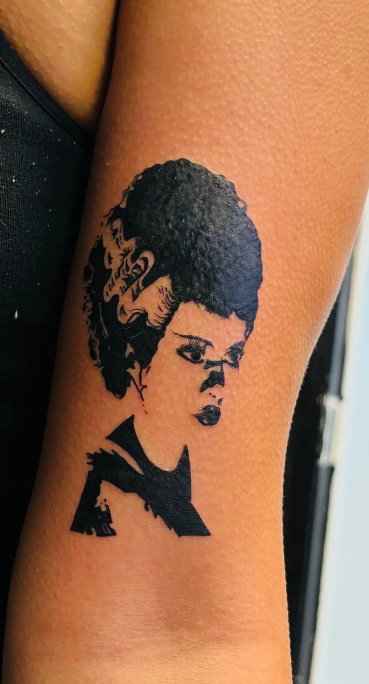 Tattoo of a woman's face with short, curly hair, dark lipstick, and a serious expression.