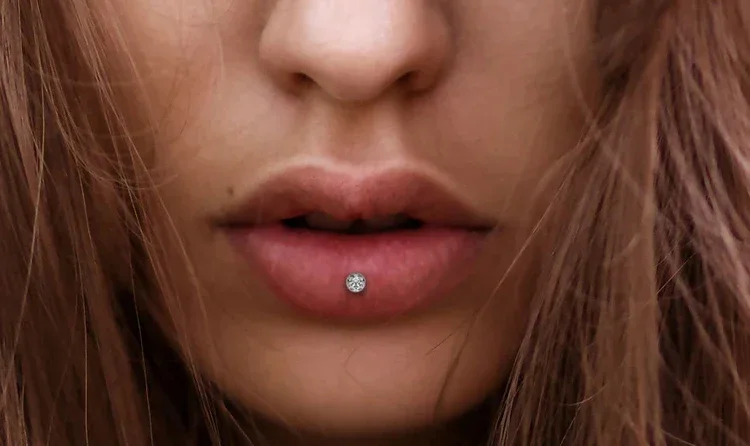 Close-up of a woman's lips with a lip piercing, and brown hair partially covering her face.