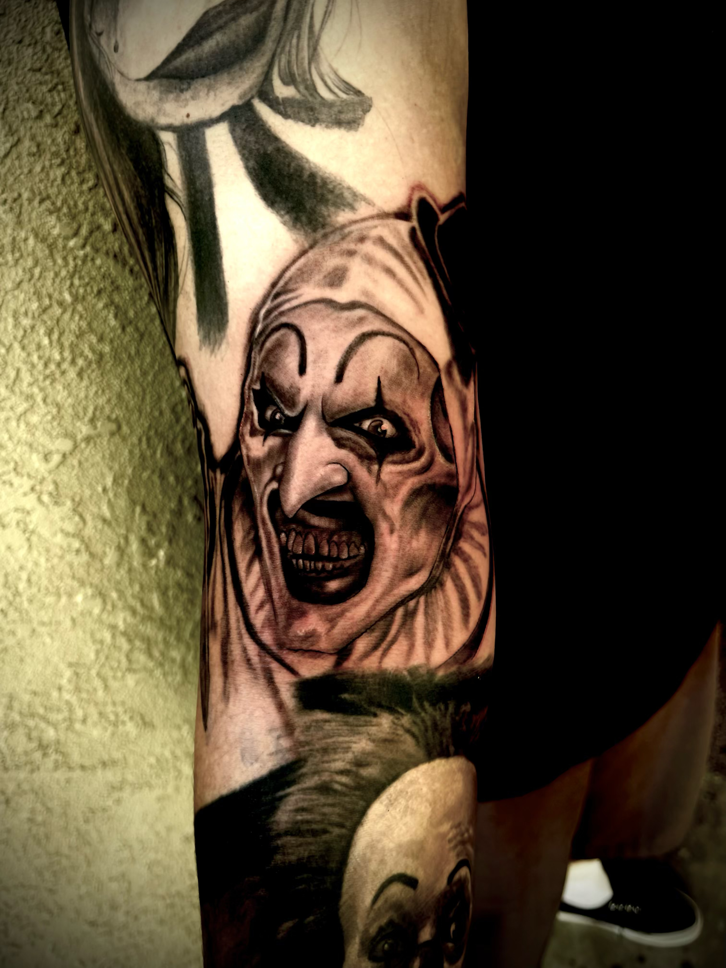 Tattoo of the Terrifier the clown's face, with an angry expression, on a person's arm.