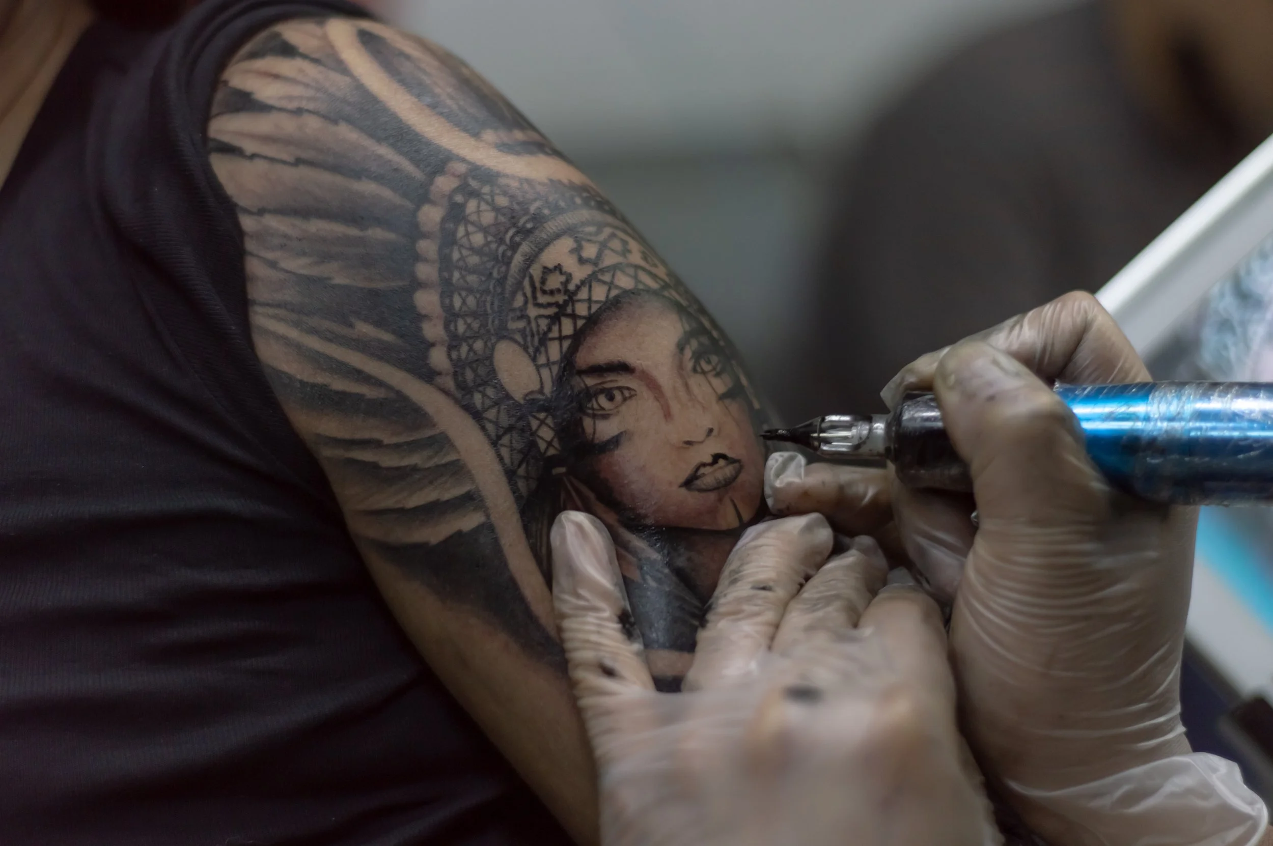 Tattoo artist creating a detailed tattoo of a woman's face and a dreamcatcher on a person's arm.