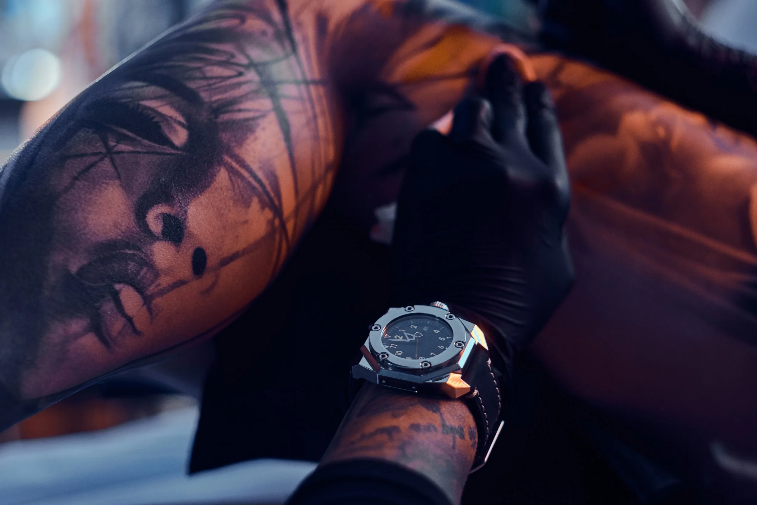 Close-up of a person's arm with a tattoo, wearing a black glove, and a watch on the wrist.