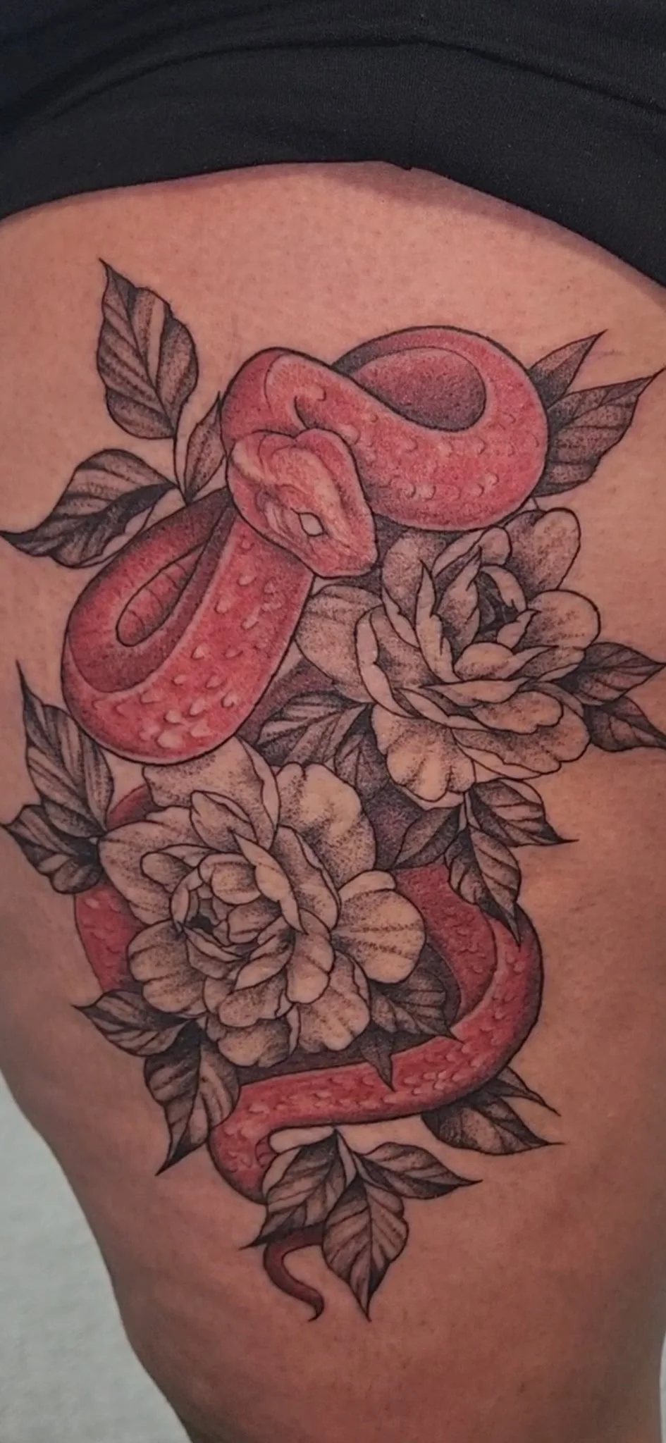 A tattoo of a snake intertwined with flowers and leaves on skin.
