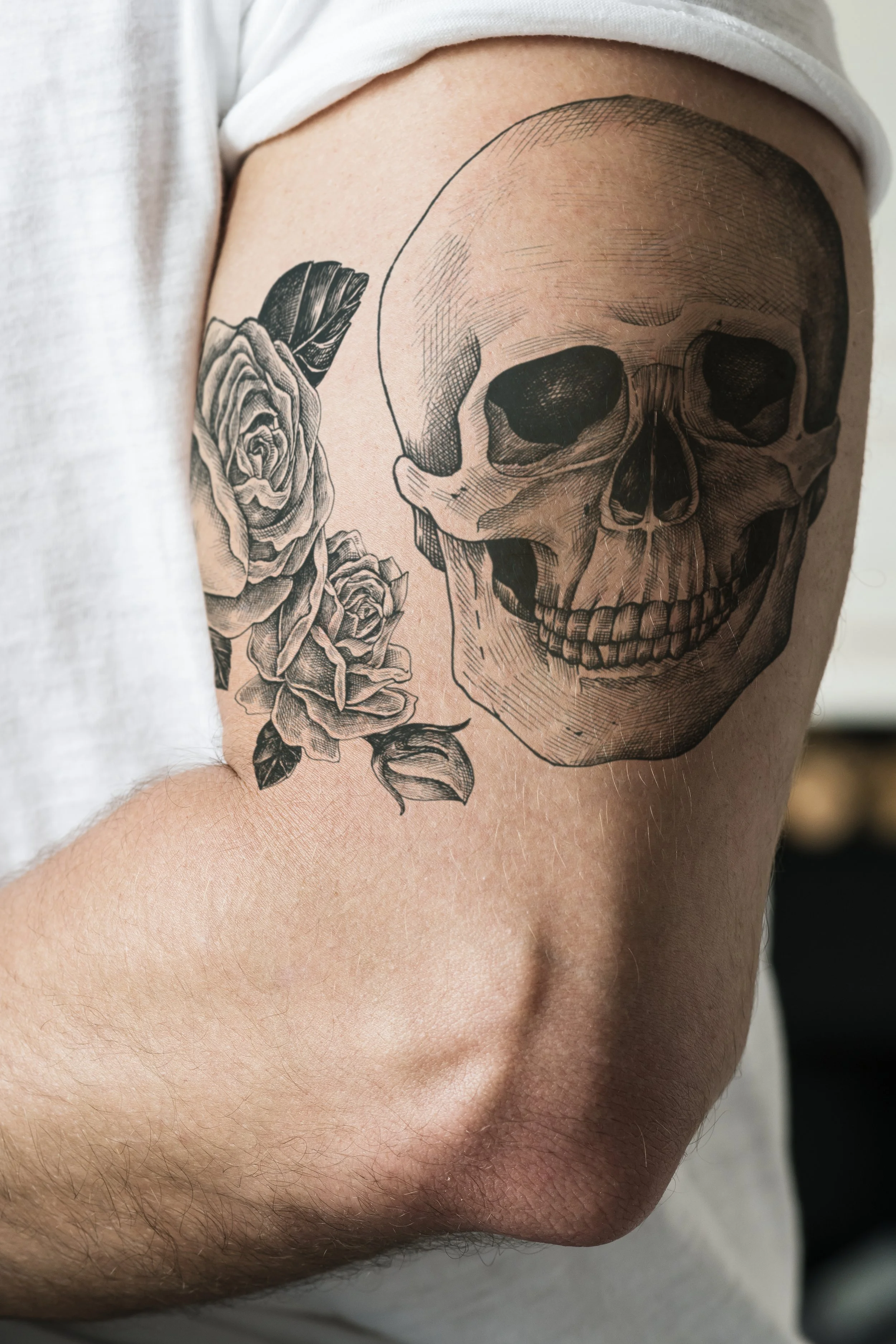 Tattoo of a human skull with roses on the shoulder.