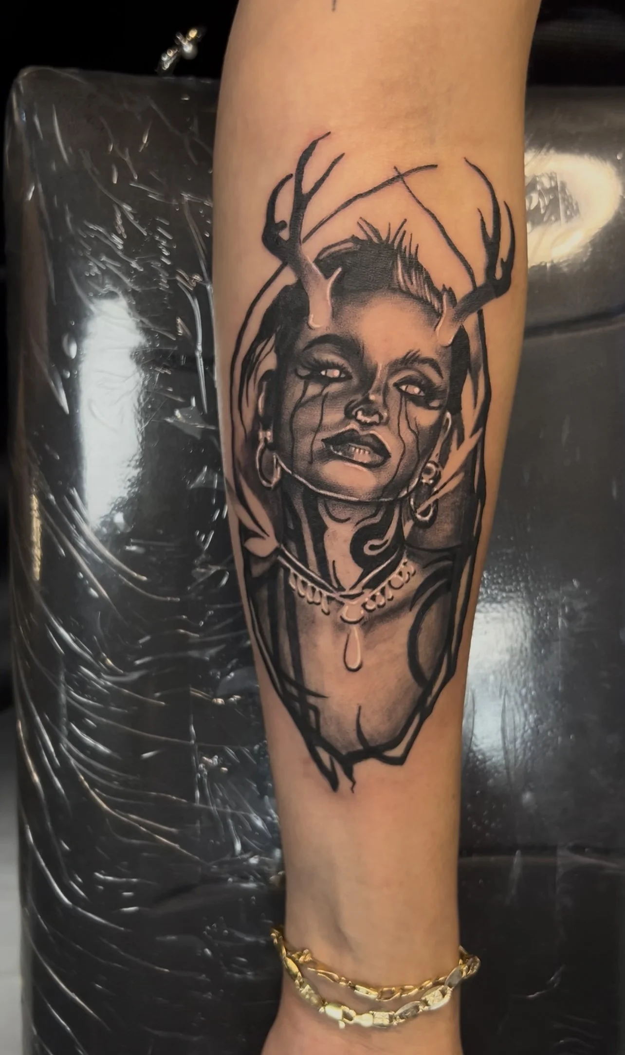 Black and gray tattoo of a woman with antlers, jewelry, and tears on her face.