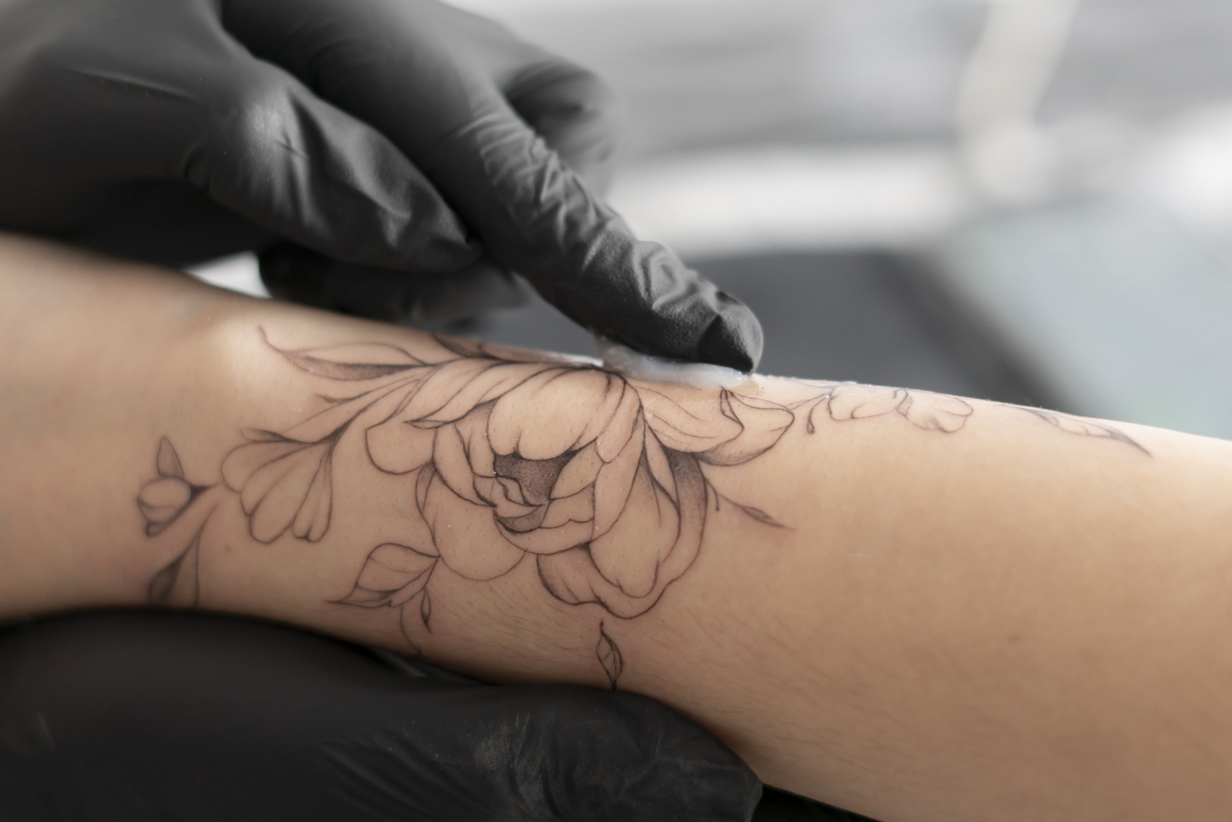 Close-up of a tattoo being inked on someone's arm, with a tattoo artist wearing black gloves applying ink.