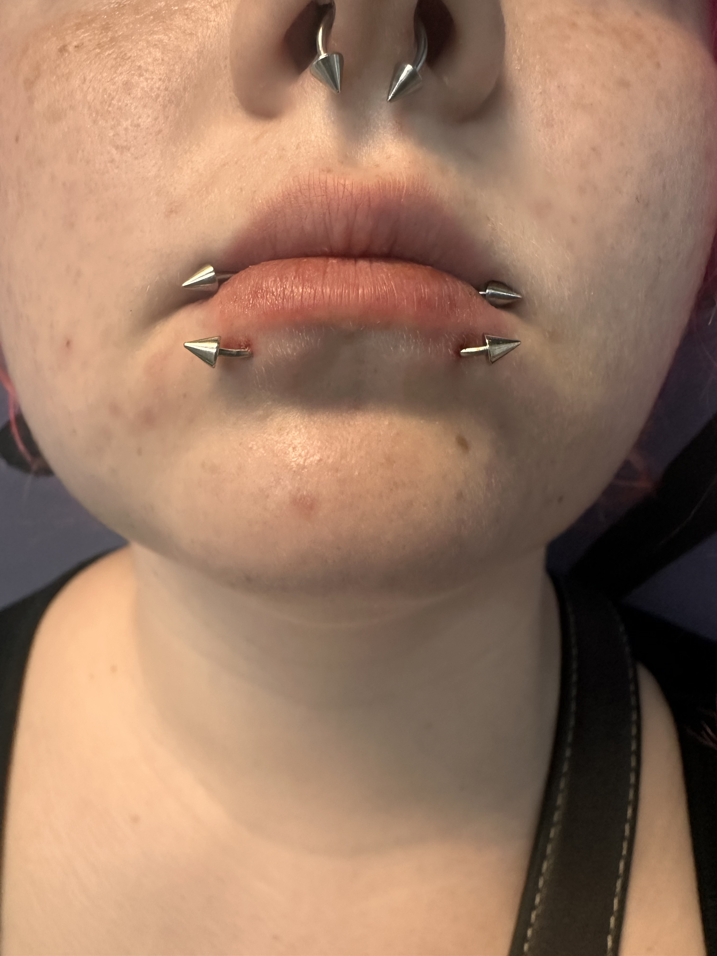 Close-up of a person's face showing pierced lips and nose with metallic jewelry, including stud and spike piercings.