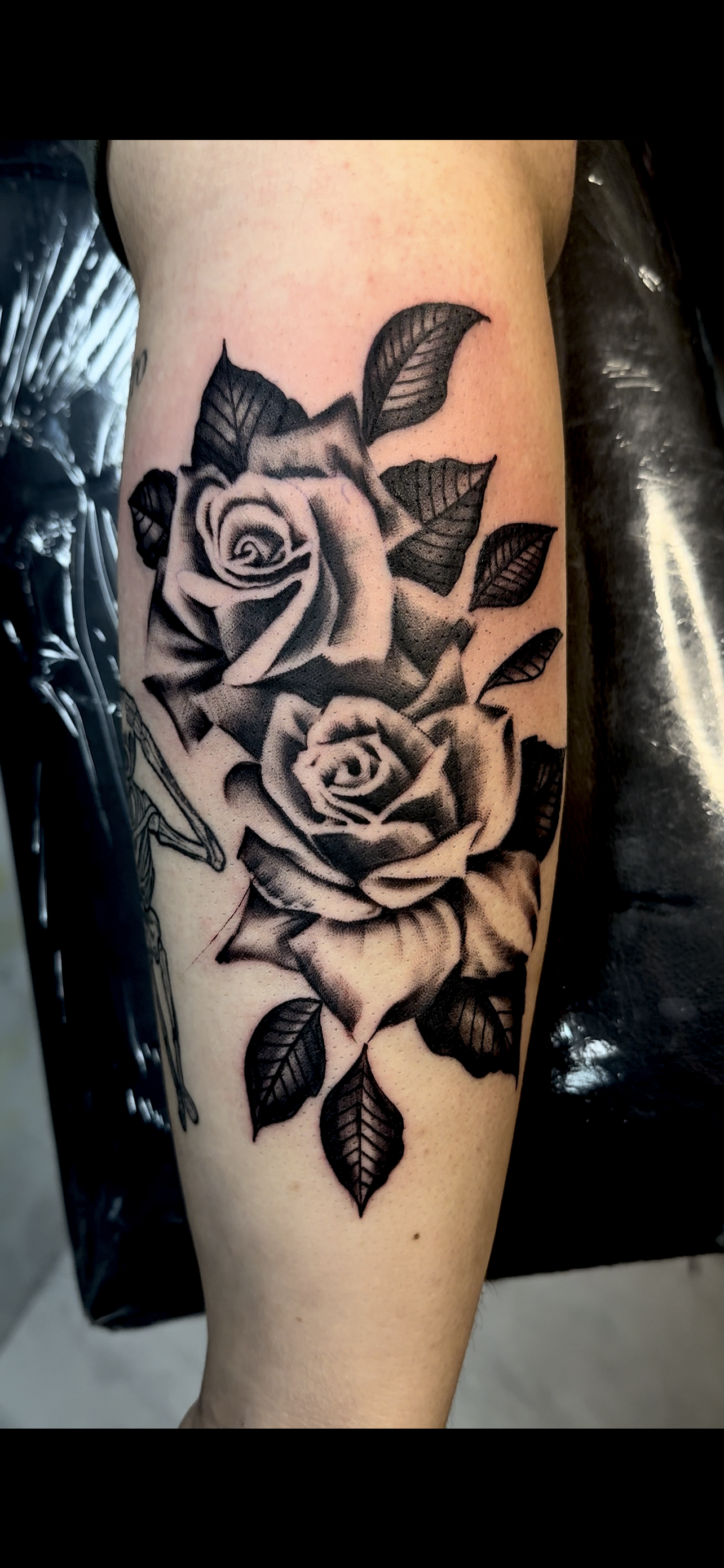 Black and gray tattoo of two roses with leaves on the person's upper arm.