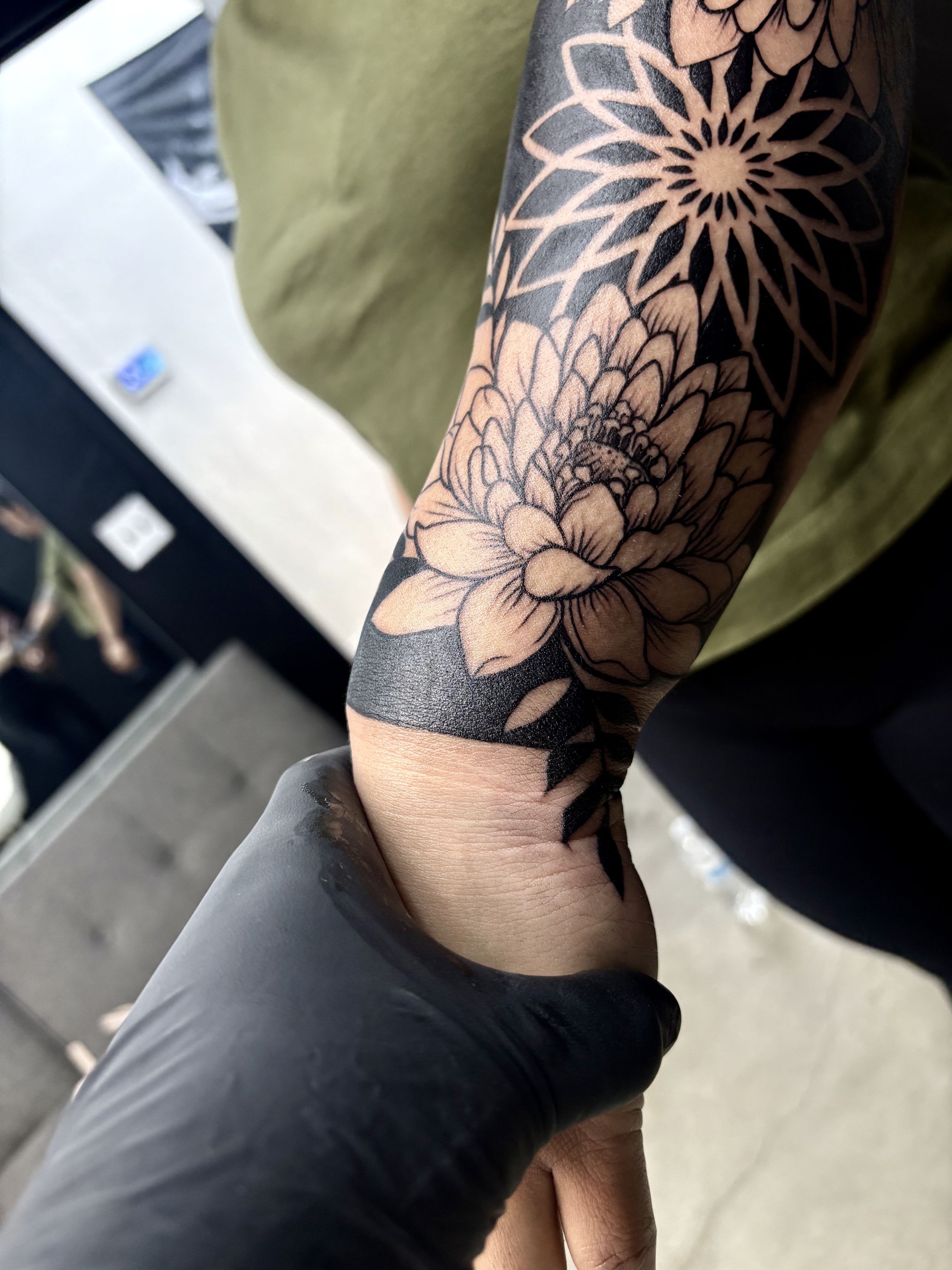 A tattoo of floral patterns on a person's arm, held by another person's hand wearing a black glove.
