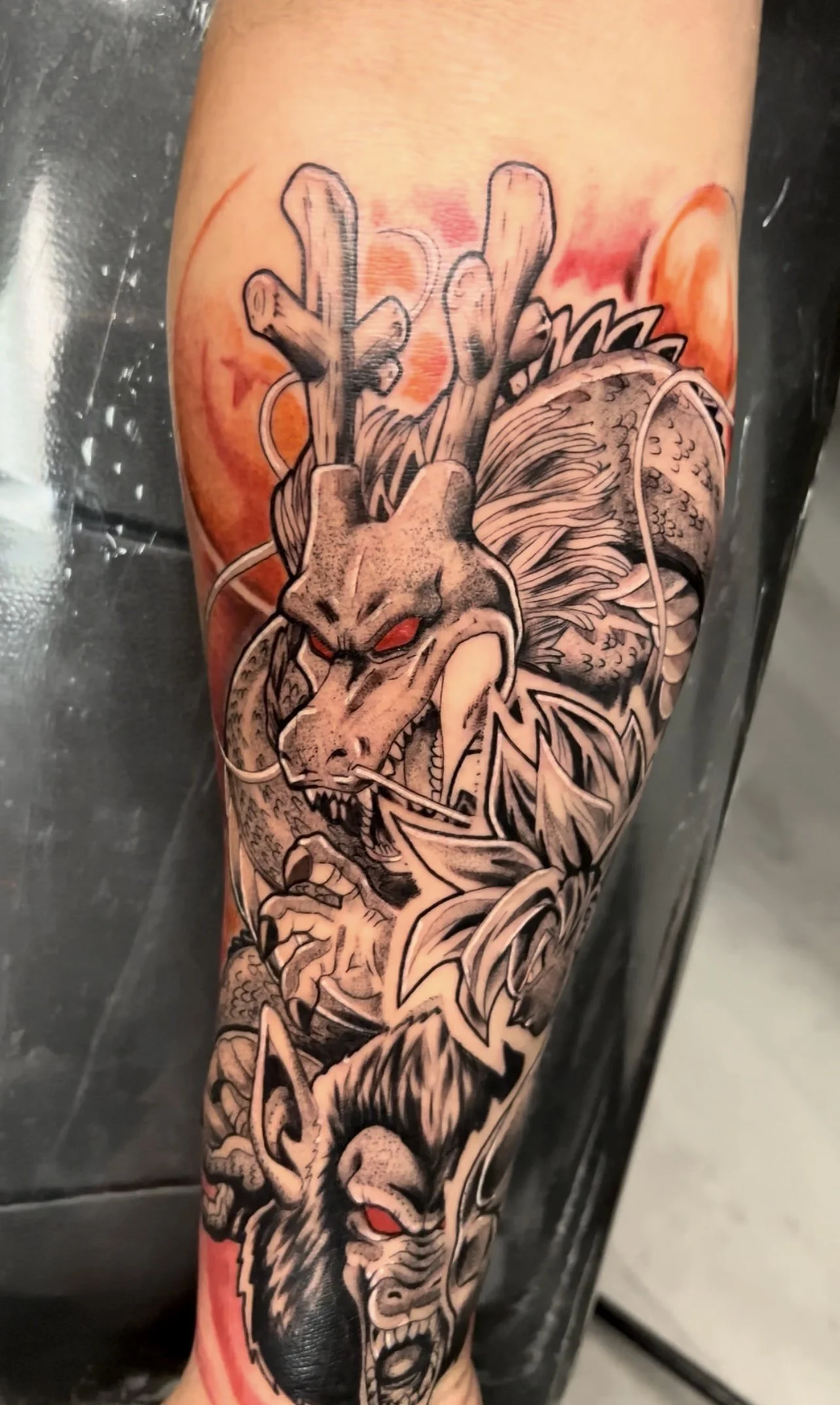 Tattoo of a fierce dragon and wolves with red eyes on a person's arm.