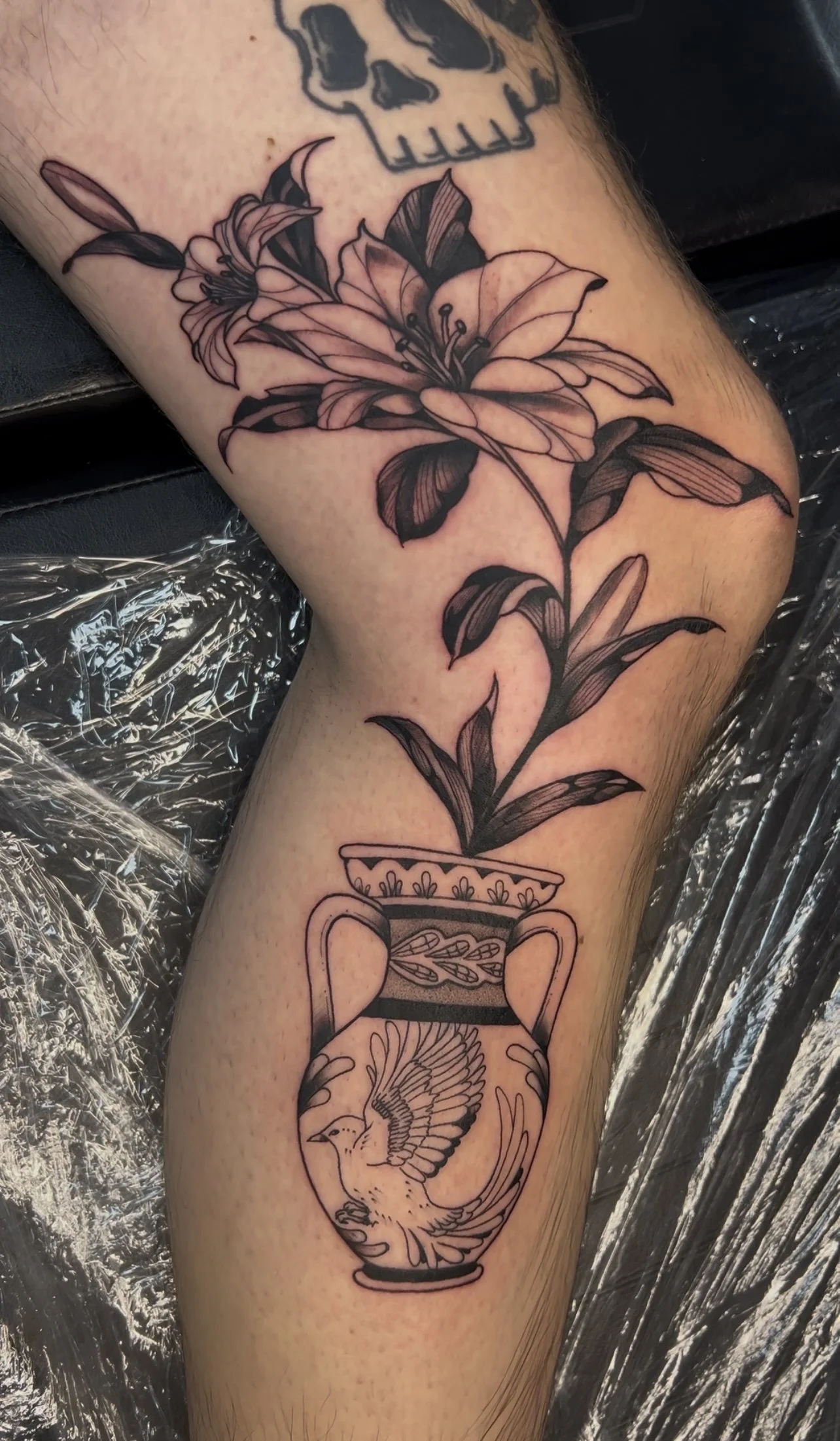 Tattoo of a flower growing from a decorative vase, with a bird inside the vase.