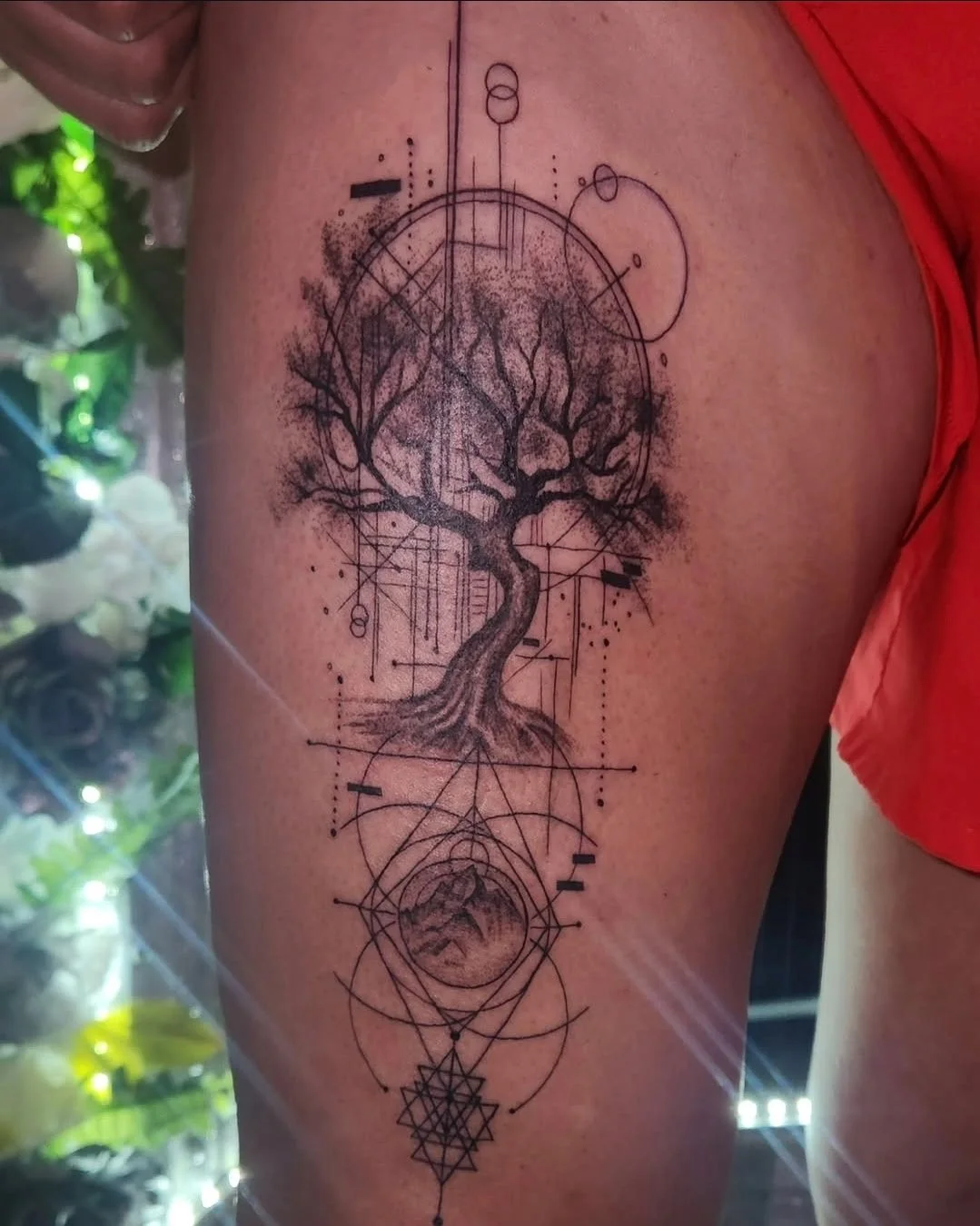 Tattoo of a tree with bare branches and roots, combined with geometric shapes, circles, and lines.