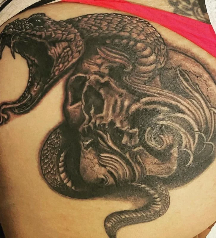 Close-up of a black and gray snake tattoo intertwined with a skull tattoo on a person's skin.
