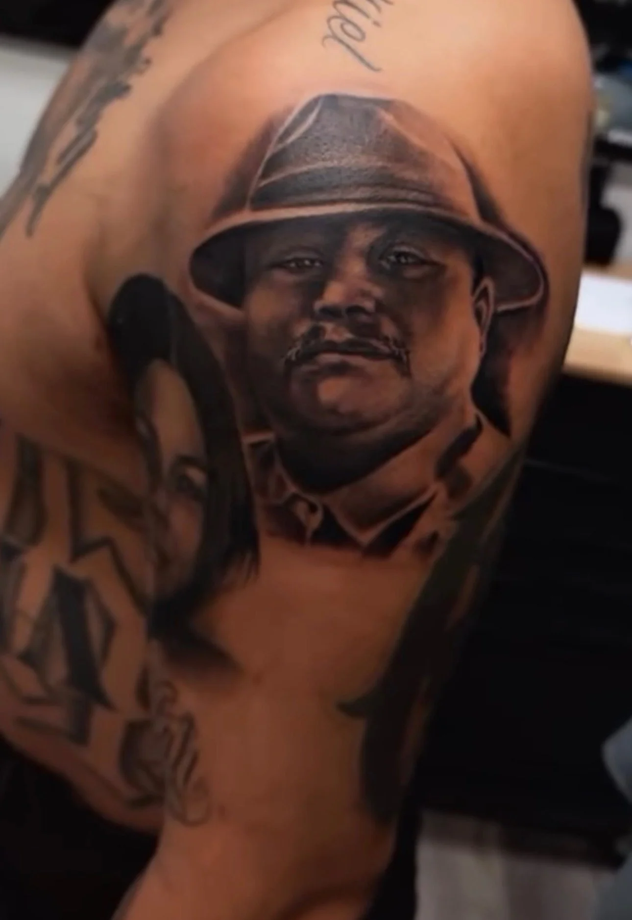 Tattoo of a man wearing a hat on a person's shoulder.