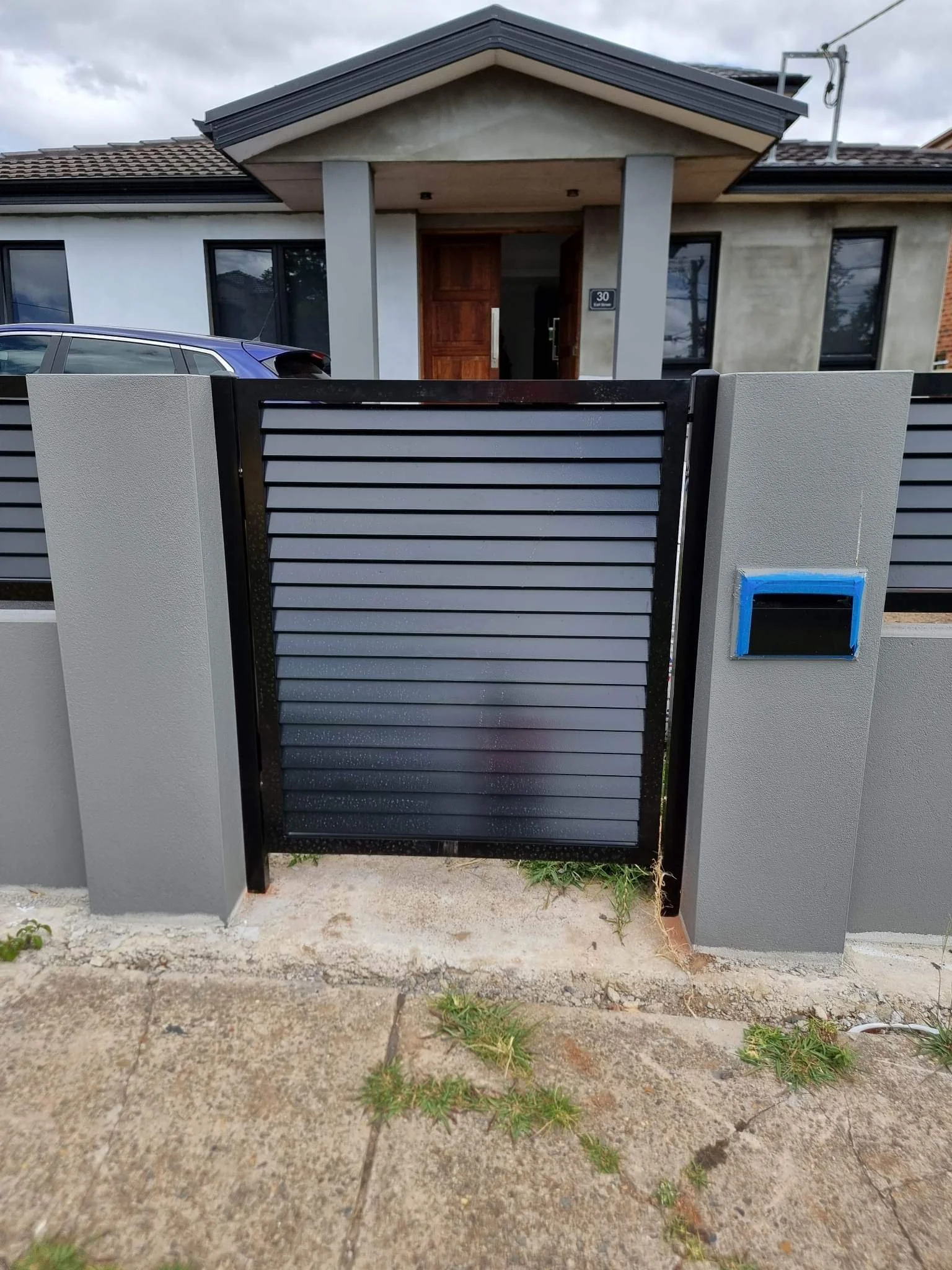 Front view of a modern house with a black metal gate and a wooden front door, with a car parked beside the gate.