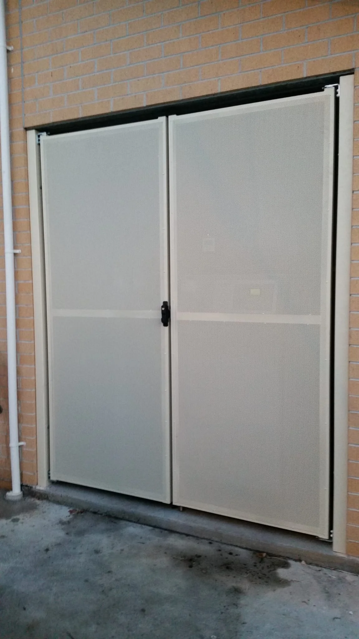 A metal door with a lock, installed on a brick wall, possibly an outdoor utility or storage closet.