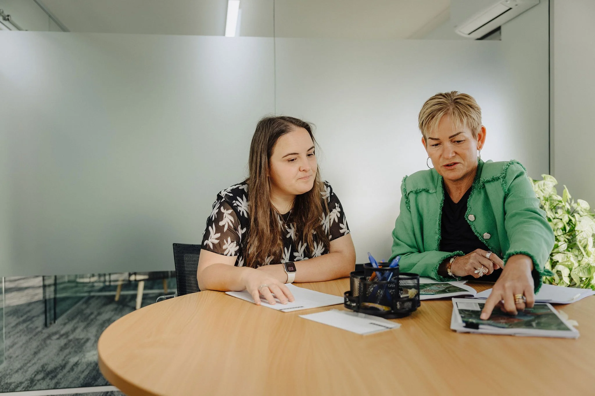 Two women sitting at a conference table discussing documents in a modern office.