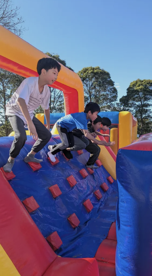 Four children climbing on an inflatable bounce house with bright colors, outdoors on a sunny day