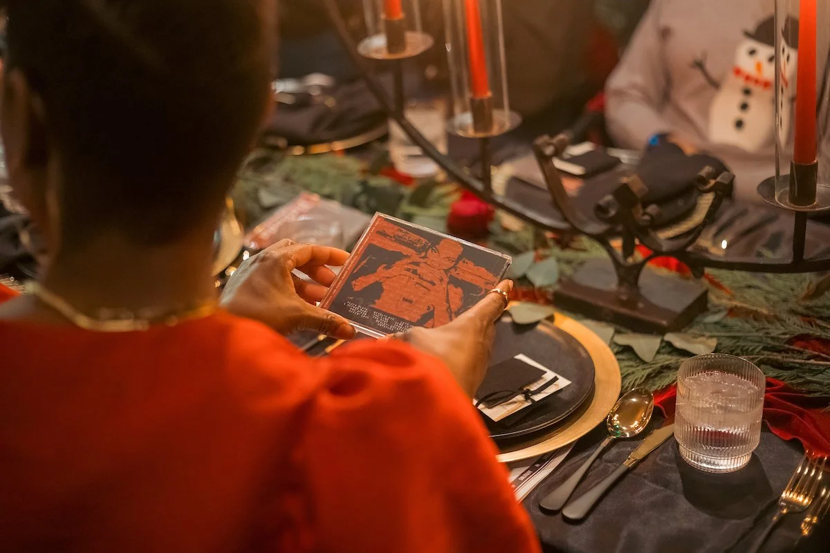 Person holding a CD or DVD case at a Christmas-themed table setting with holiday decorations and candles.