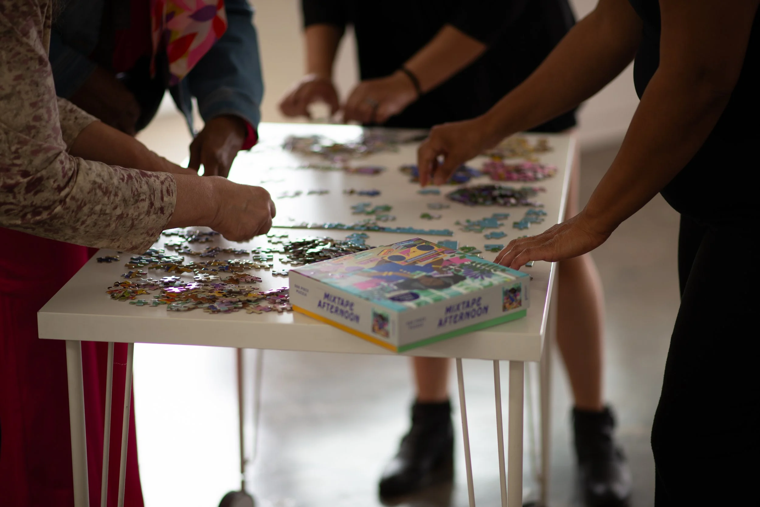People working together on a jigsaw puzzle at a white table with a box labeled 'My Puzzle Afternoon'.