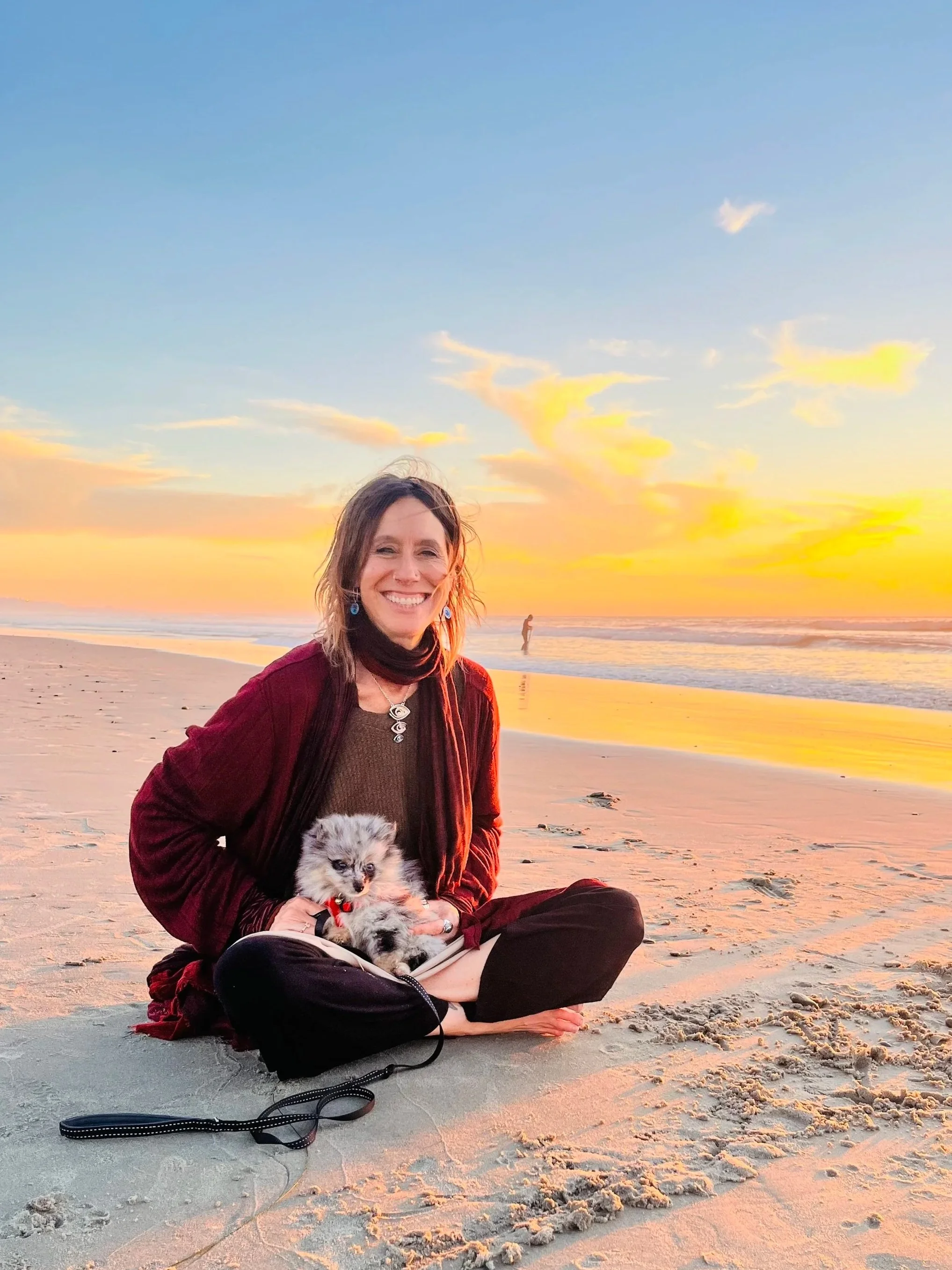 Chandra smiling at the camera on the beach with a puppy in her lap