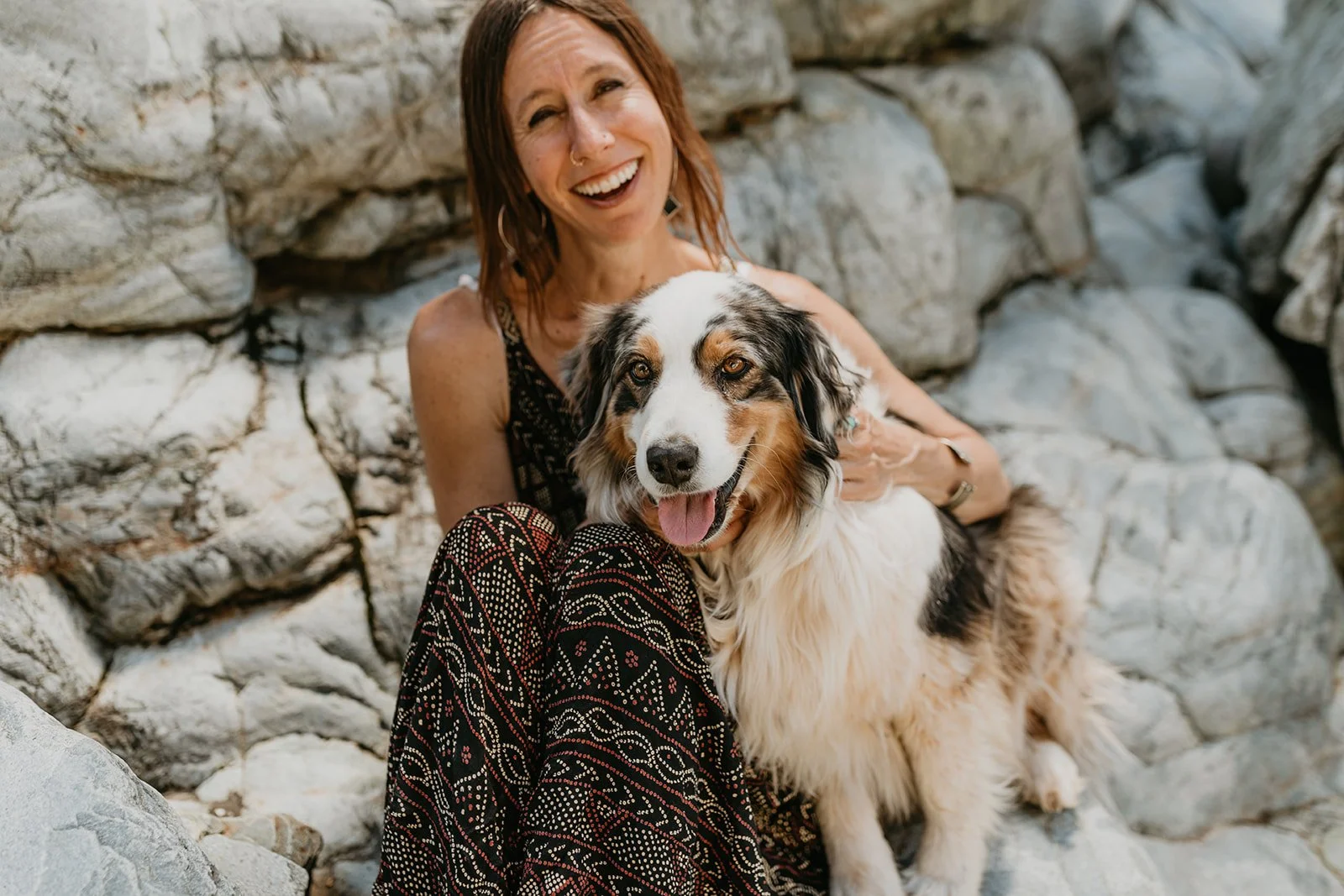 Chandra sitting outdoors and smiling at the camera with her dog