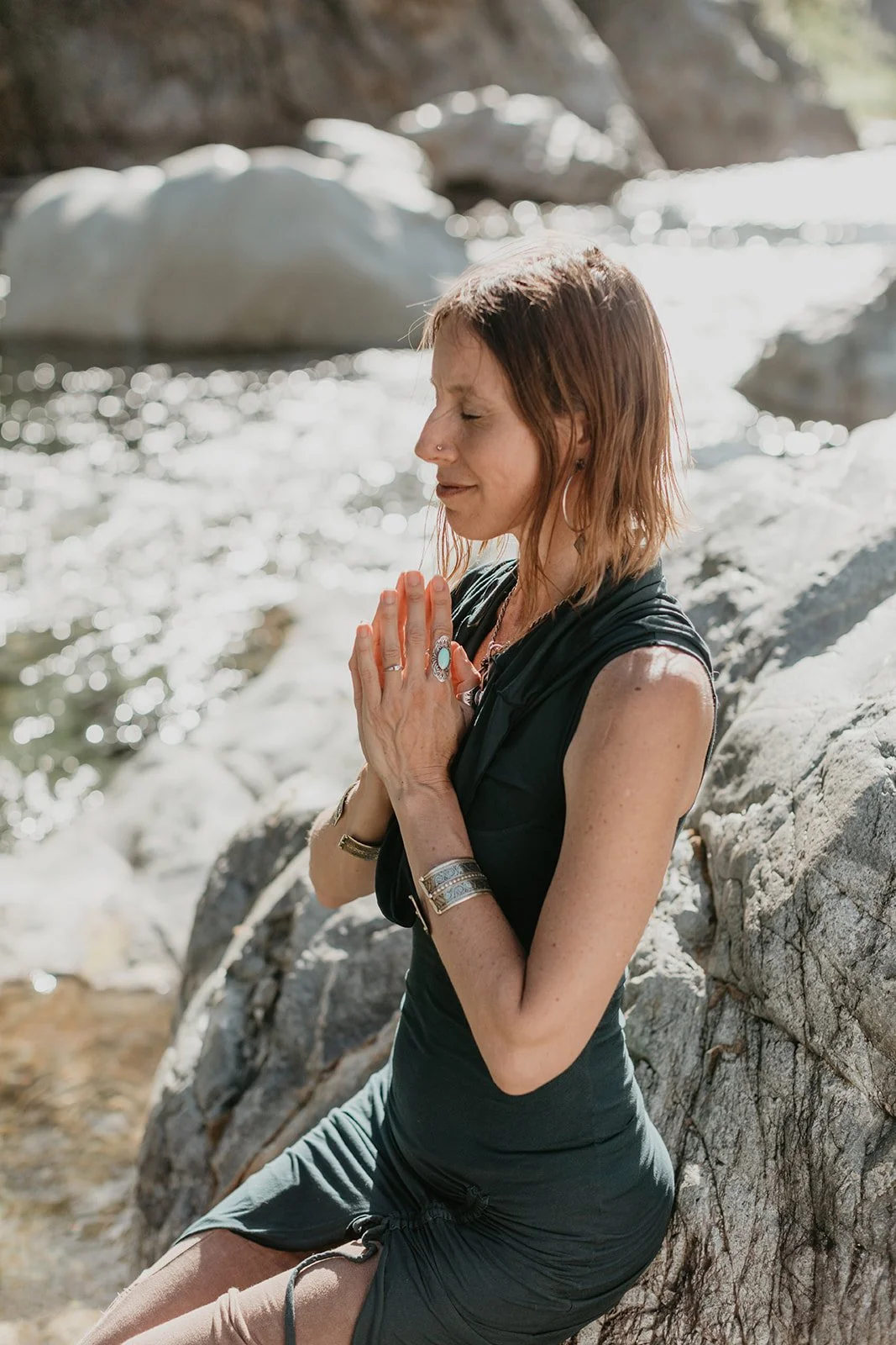 Chandra smiling in anjali mudra near a river