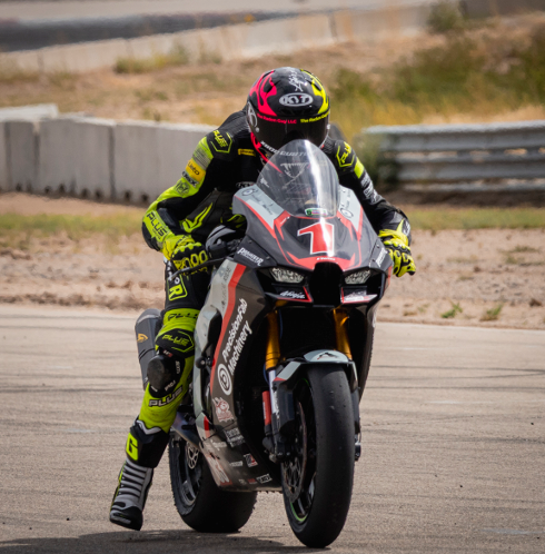Motorcycle racer in racing suit and helmet riding a black and red motorcycle on a race track.
