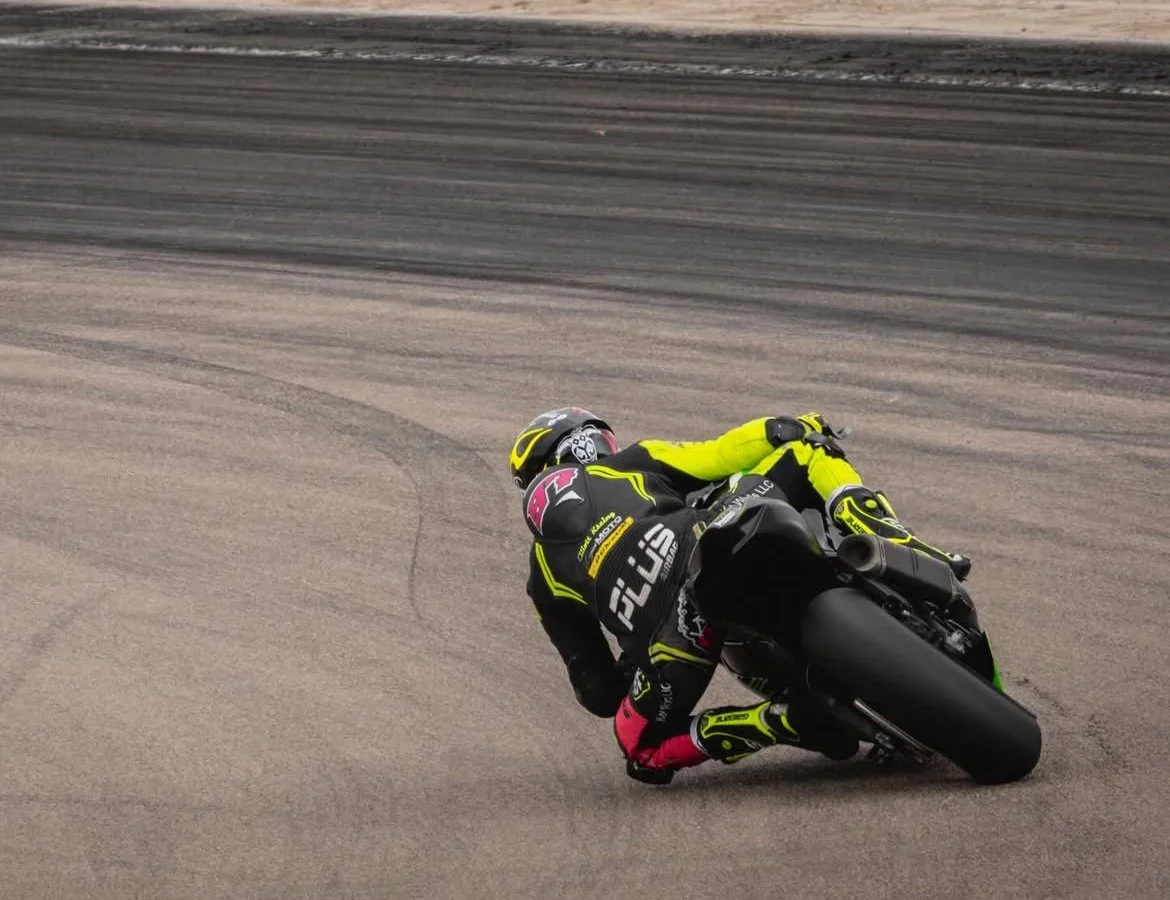 Motorcycle racer leaning into a turn on a racetrack, wearing a black and yellow suit and helmet.