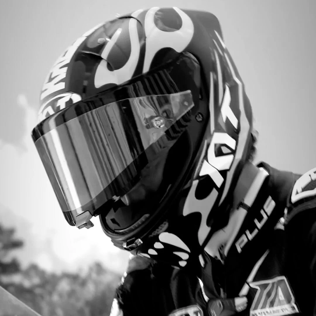 Motorcycle racer in full gear, wearing a helmet with a reflective visor.