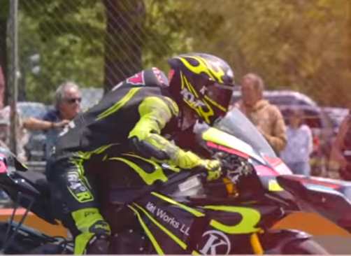 A motorcycle racer in black and yellow gear leaning into a turn on a racetrack.