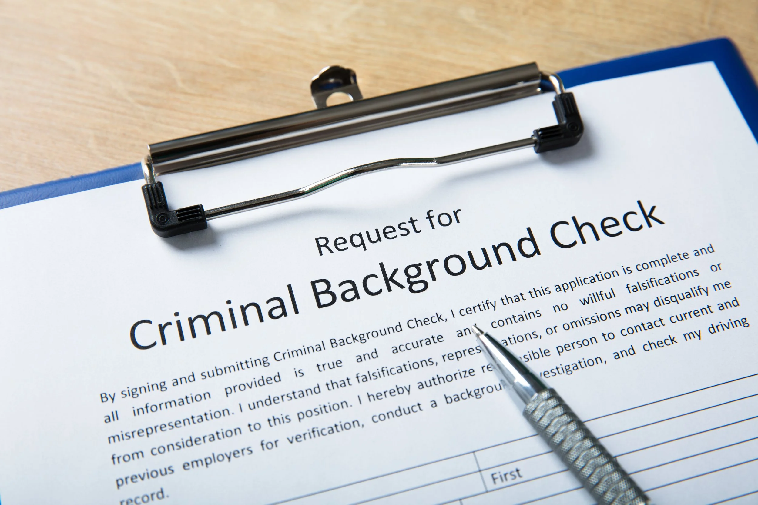 Request for criminal background check form on a clipboard with a pen and a small metallic tool.