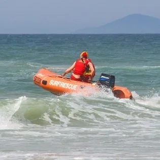 A person wearing a red life jacket and orange helmet riding an inflatable rescue boat in the ocean.