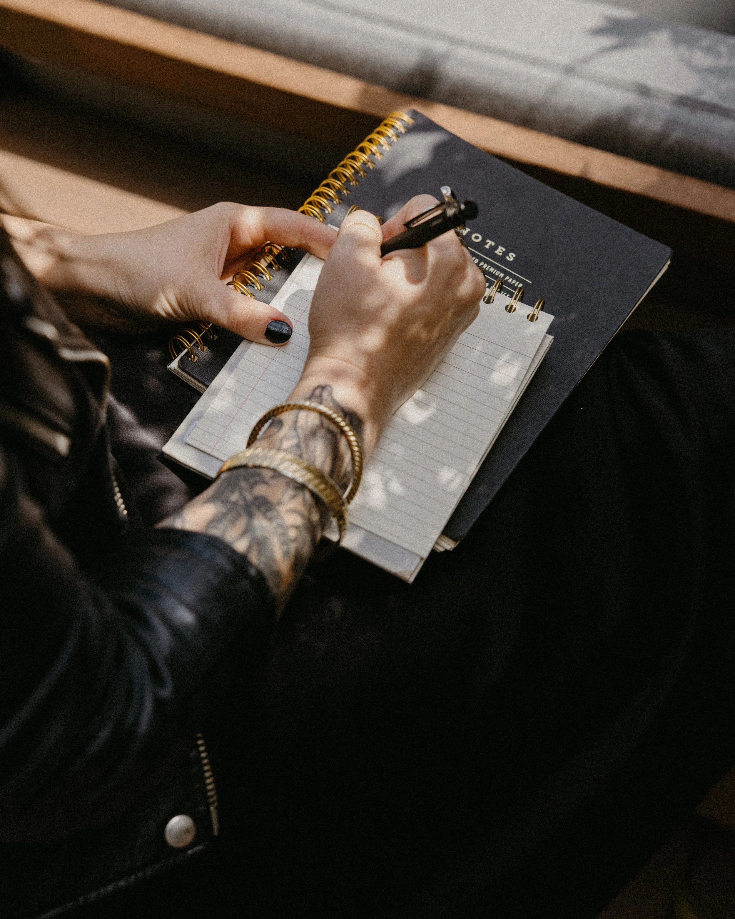 zina dichoso aimee from hello you studio with tattoos and gold jewelry writing in a notebook with black leather jacket
